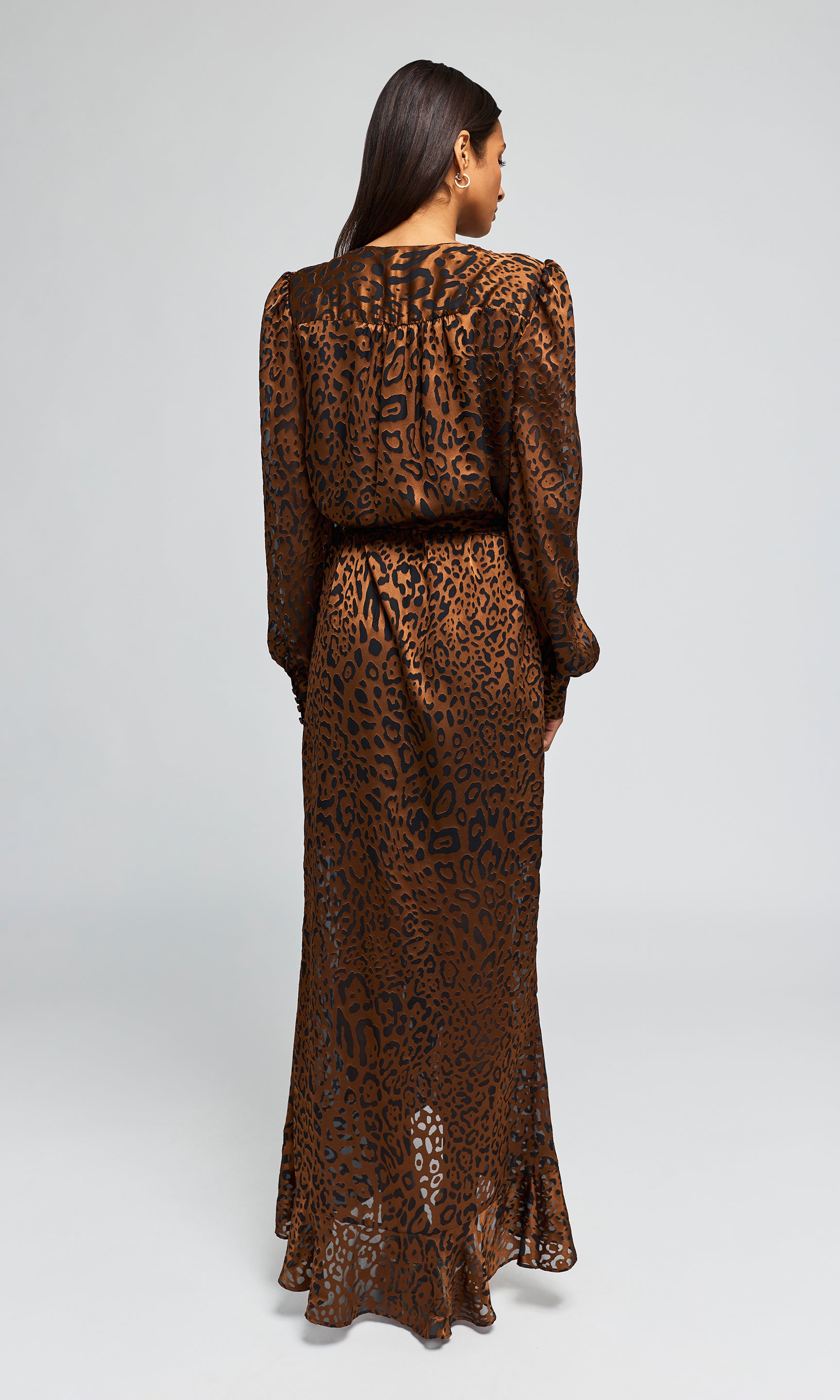 Back view of model wearing a long brown leopard-print maxi dress with a high slit, paired with clear high-heeled.