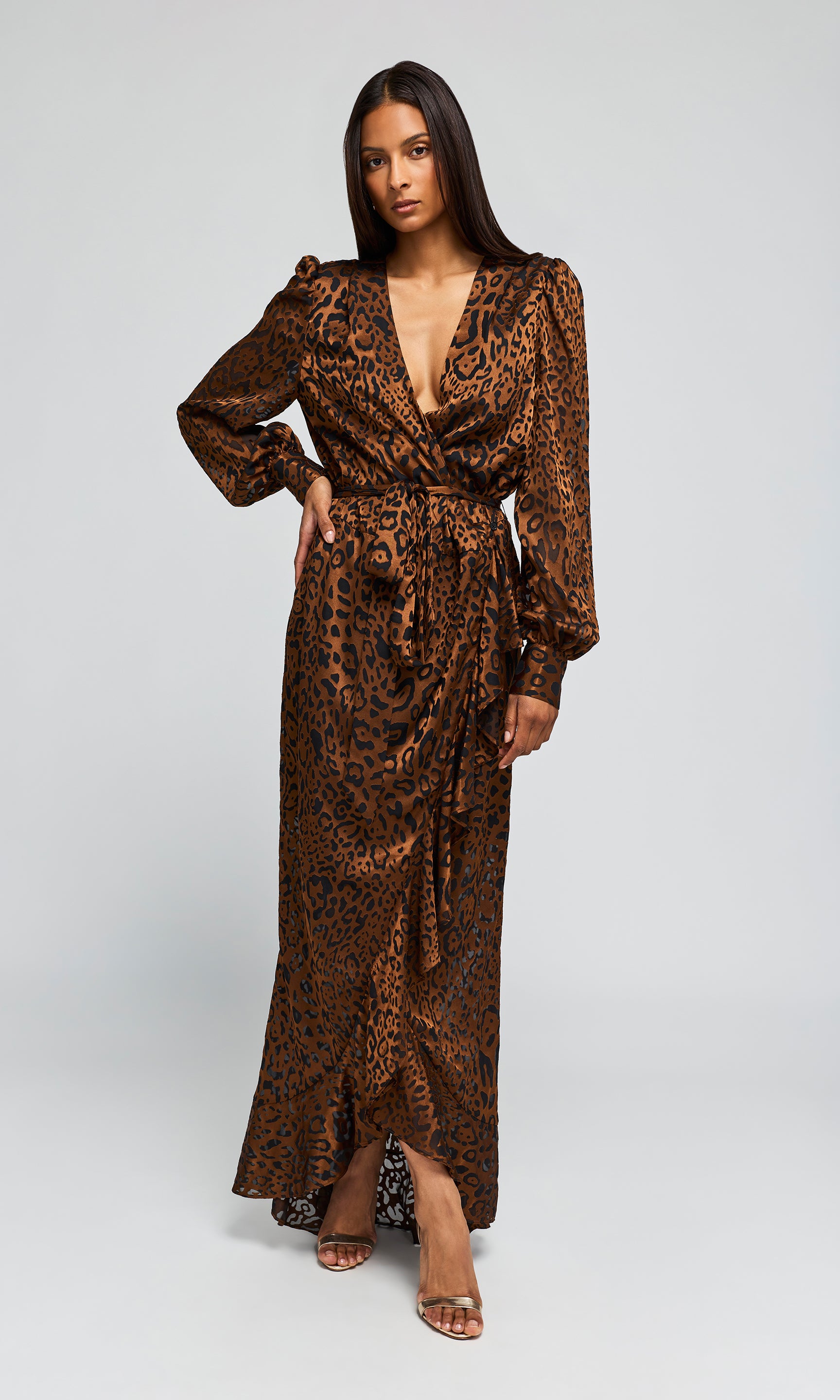 Model wearing a long brown leopard-print maxi dress with a high slit, paired with clear high-heeled.