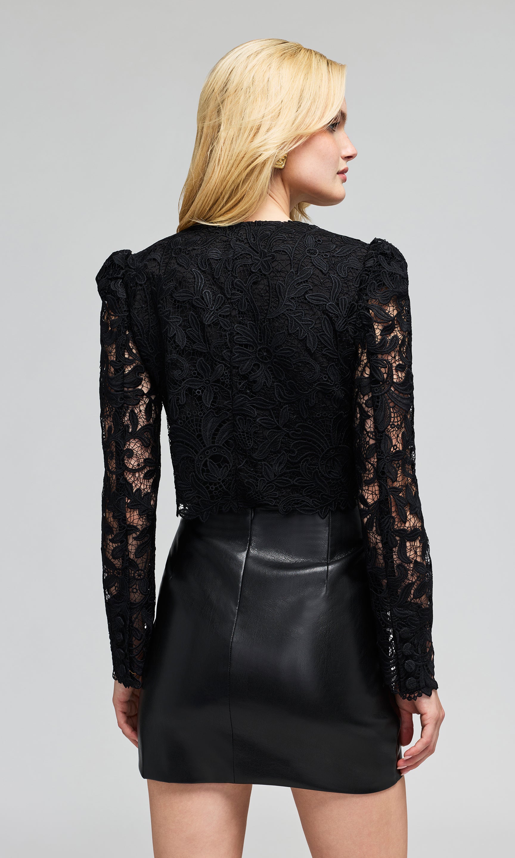 Back view of model wearing a black long-sleeve lace top with a scalloped button-front bodice and a black faux-leather wrap mini skirt.