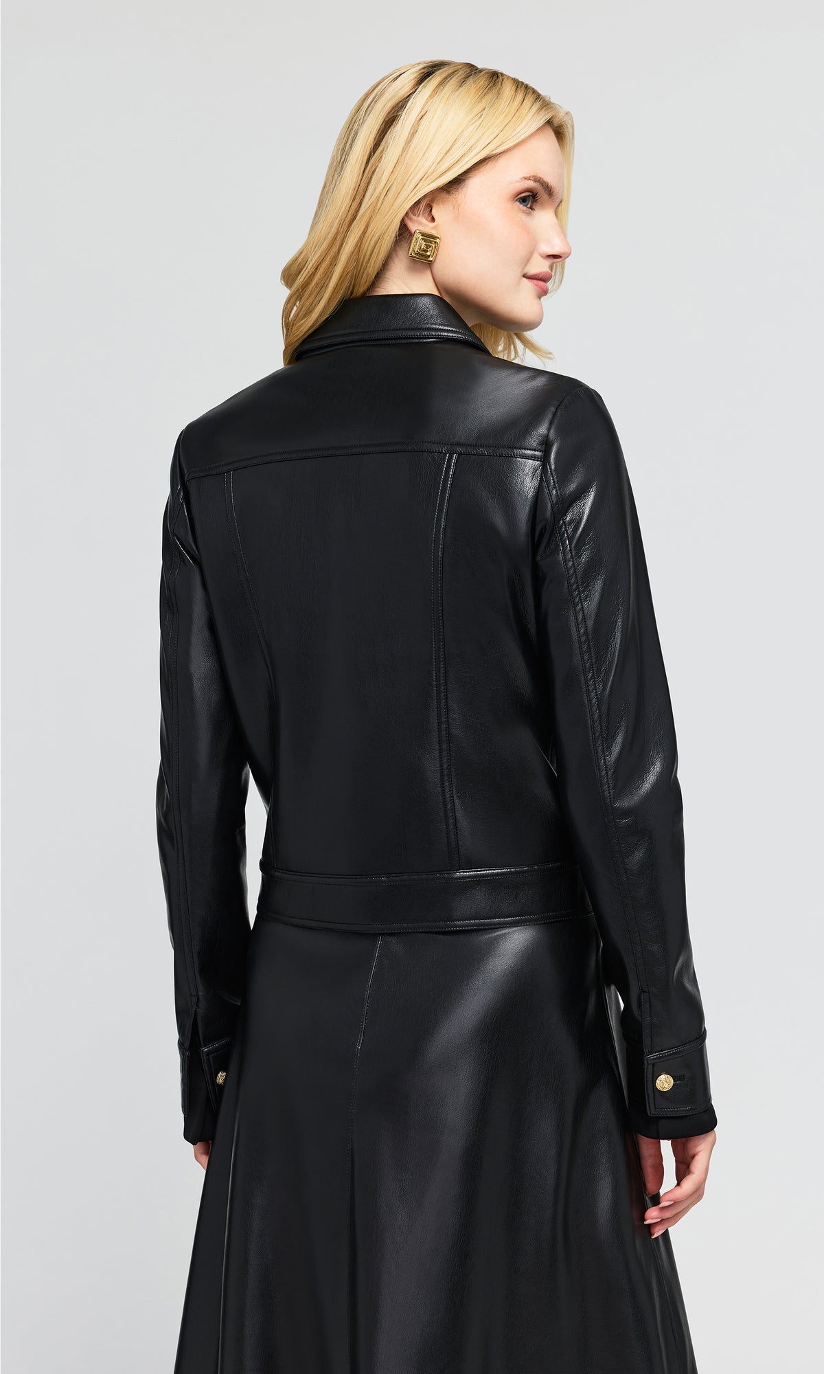 Back view of model shown from the back wearing a black faux-leather jacket and matching long skirt.