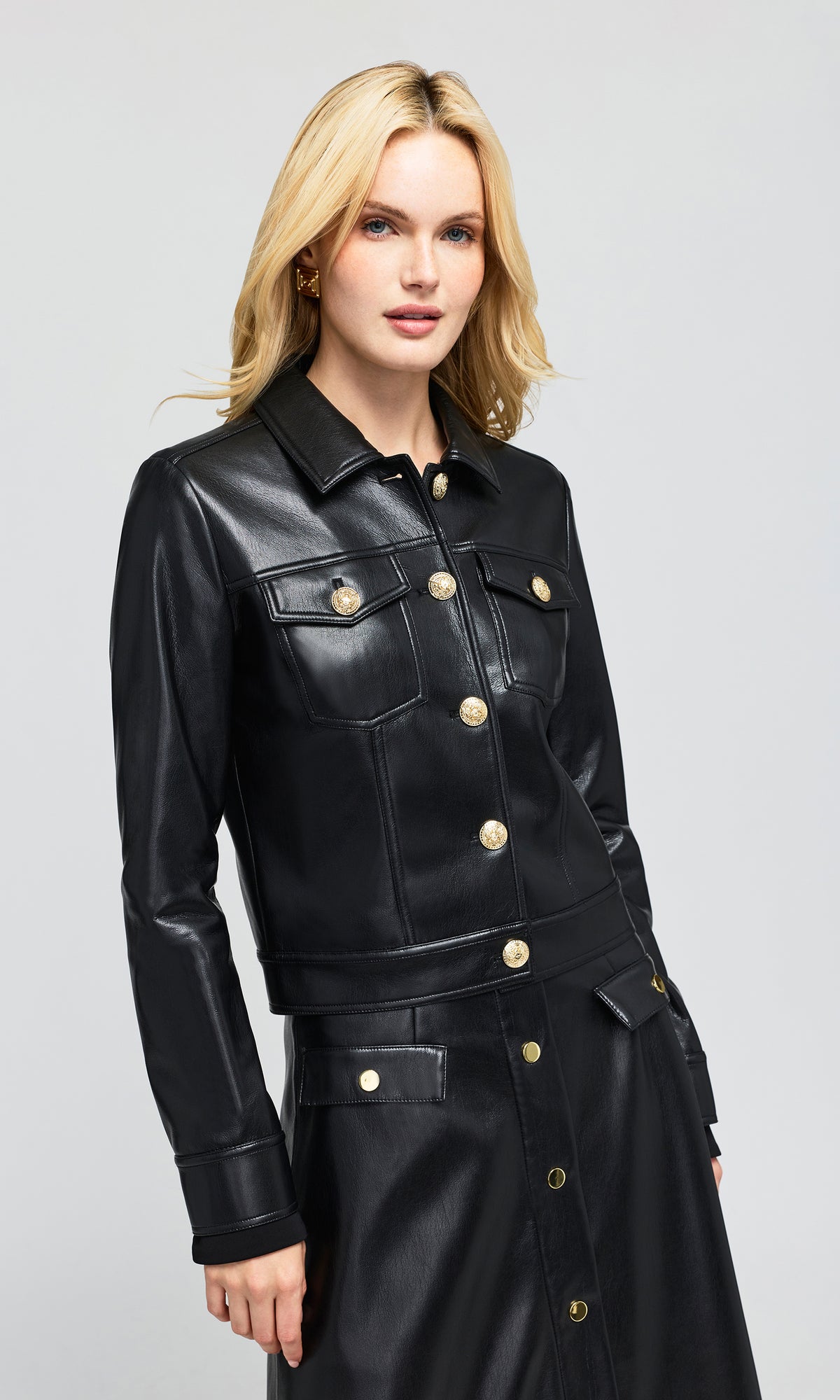 SIde view of model wearing a black faux-leather jacket with gold-tone buttons.