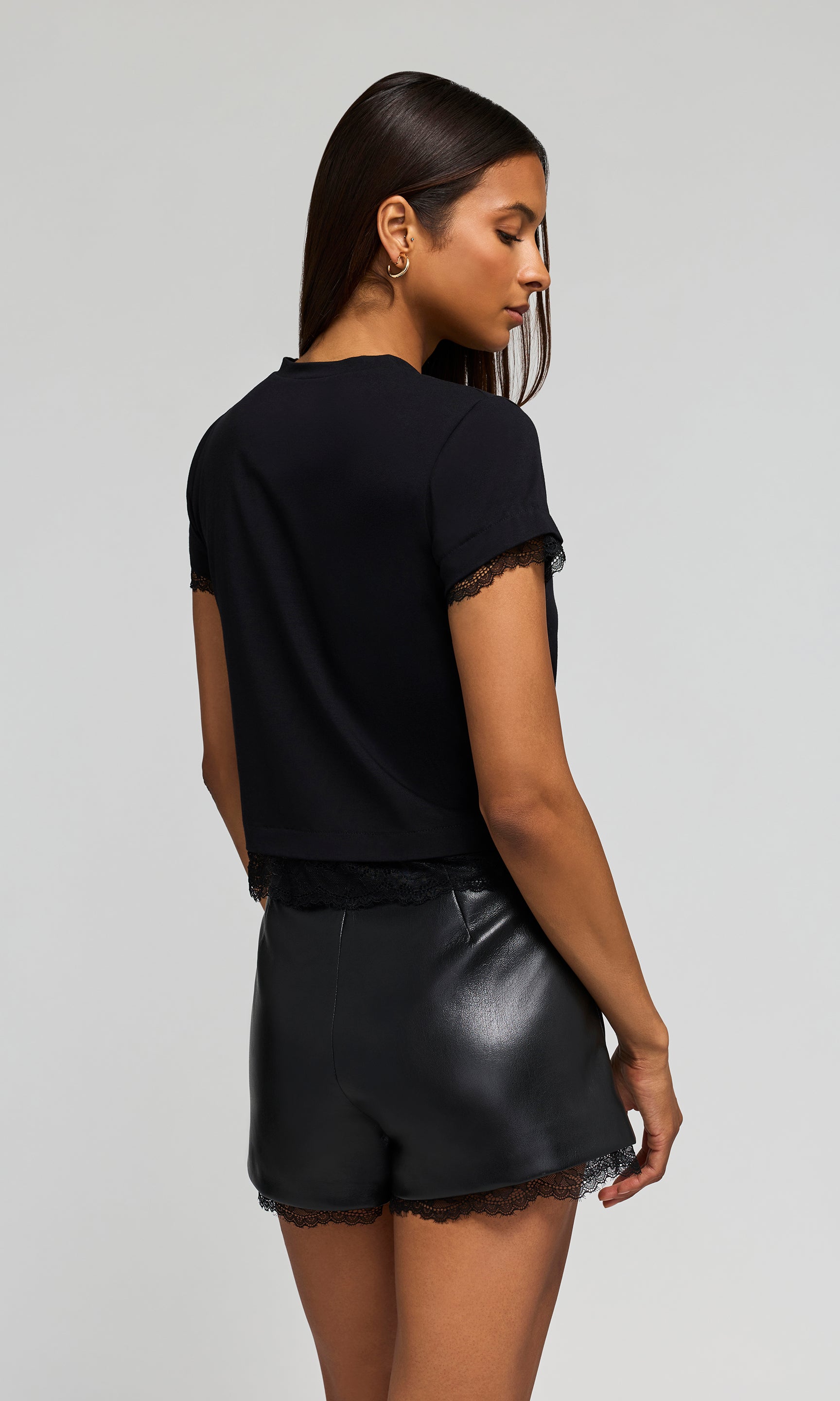 Back view of woman wearing a black top and leather shorts on a white background