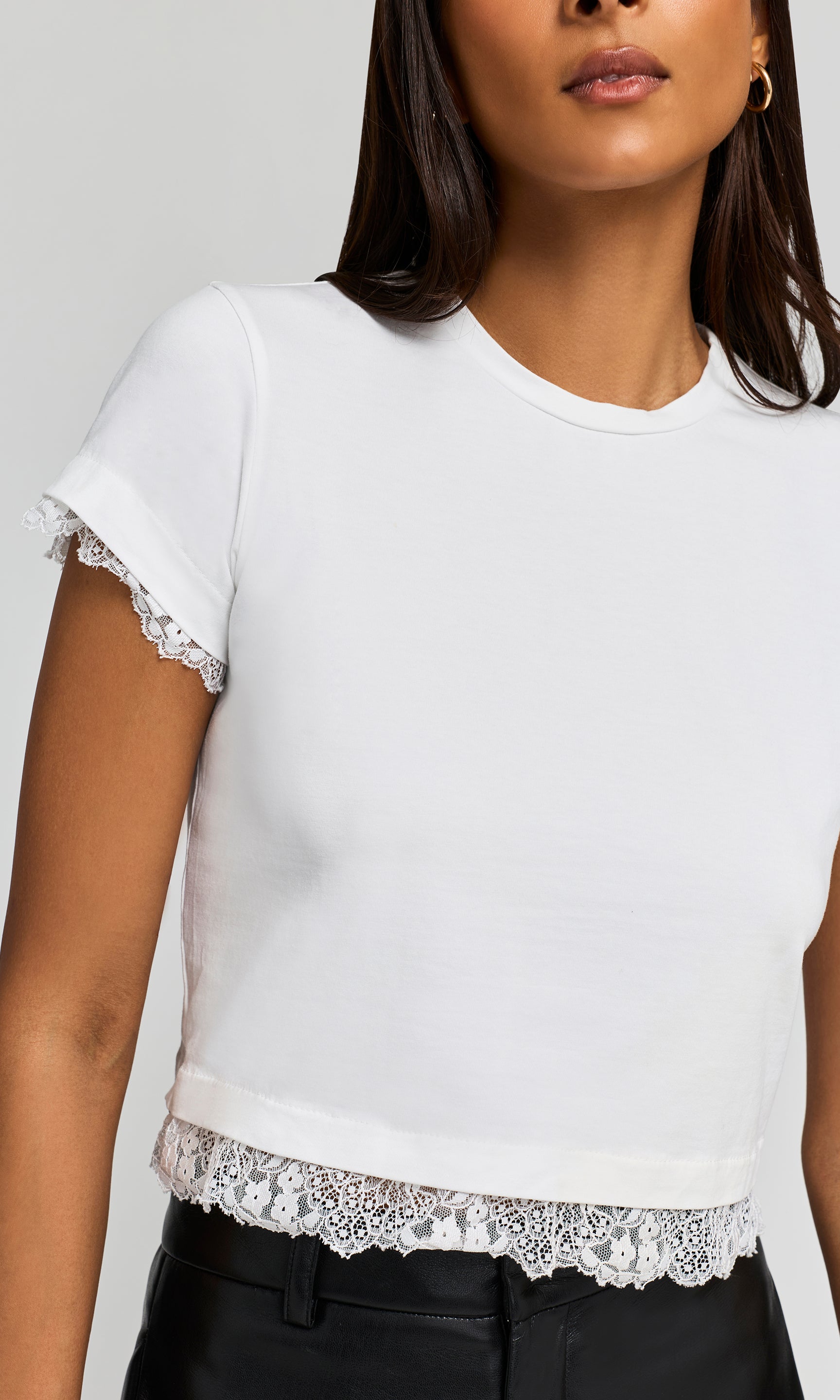 Close-up of a white short-sleeve crop top with delicate lace trim at the sleeve cuffs and hem.