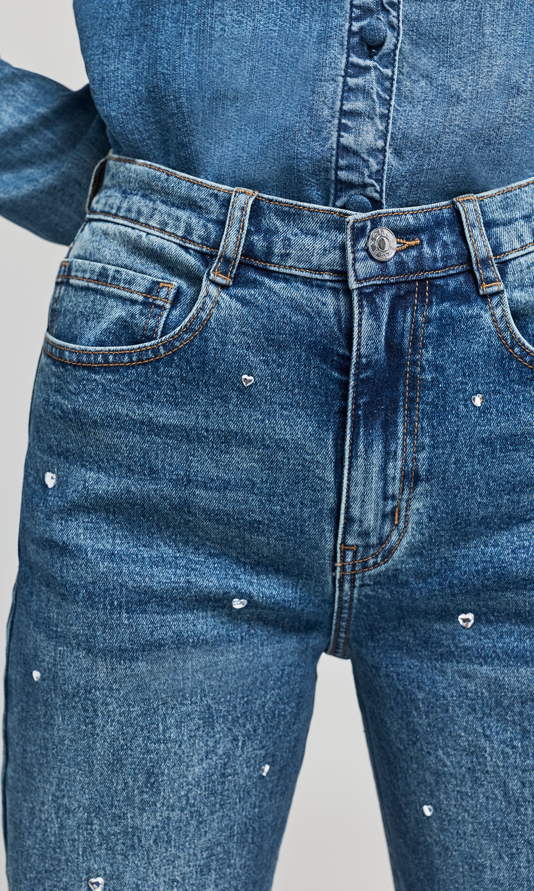 Close-up of blue denim jeans with small silver heart embellishments scattered across the front.