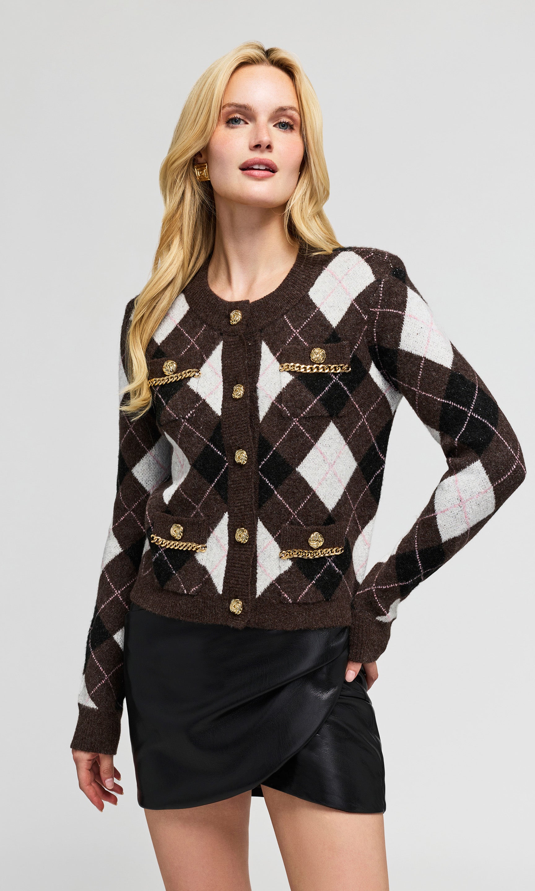 Model wearing a cropped brown argyle cardigan with gold-tone buttons and chain details, paired with a black mini skirt.