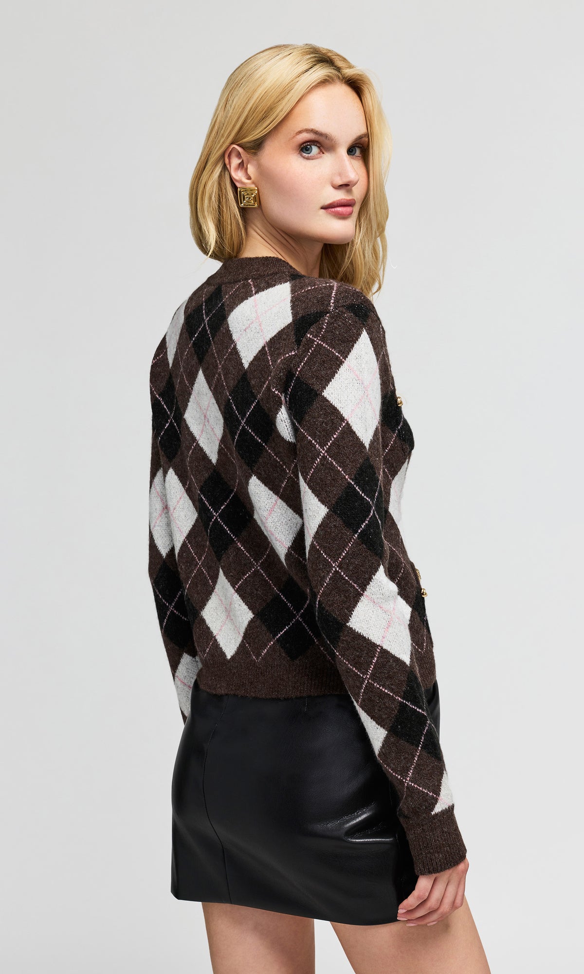Back view of model wearing a brown, black, and white argyle knit sweater, paired with a black faux-leather skirt.