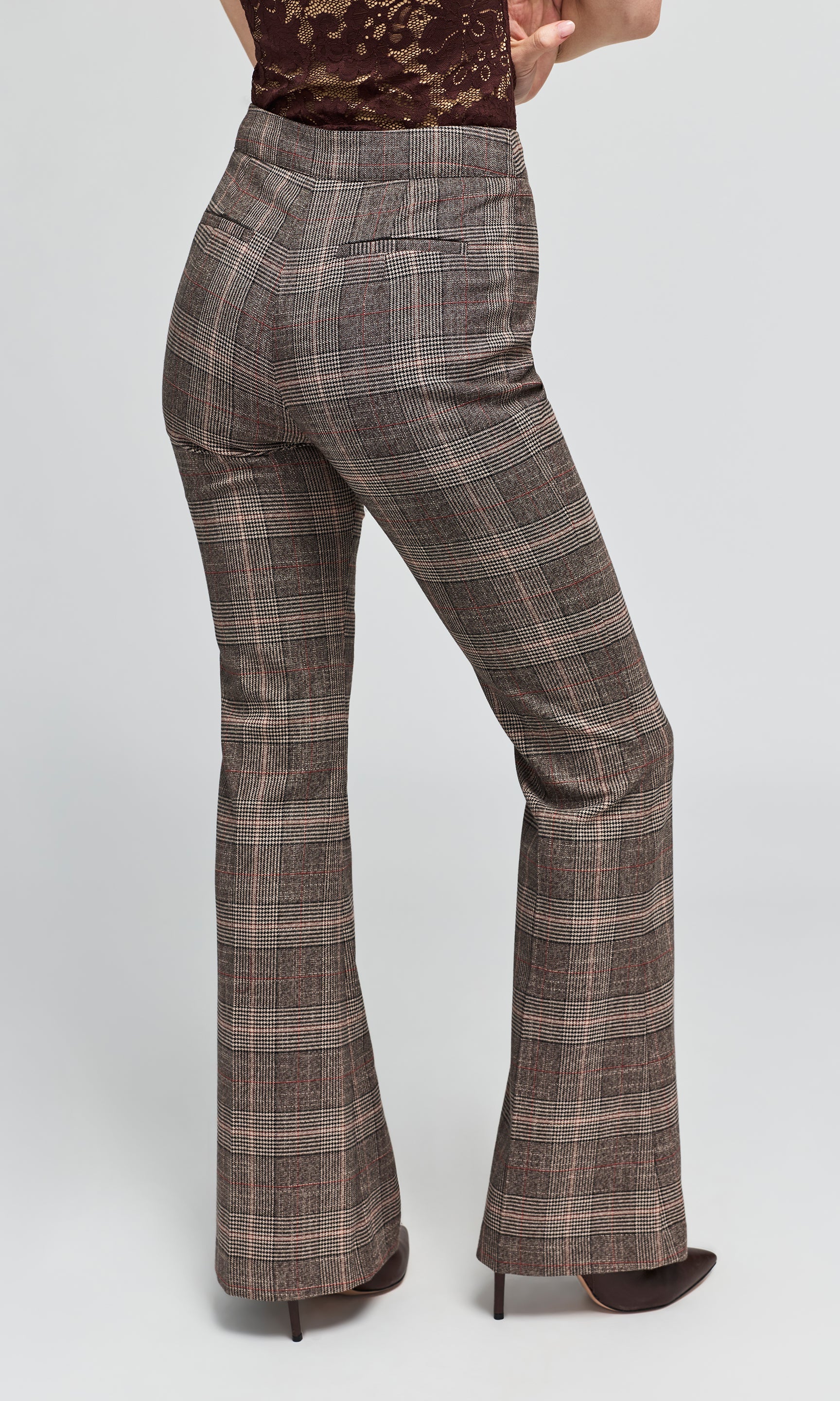 Back view of model wearing a pair of brown and gray plaid flare pants with a lace top, on a plain background.