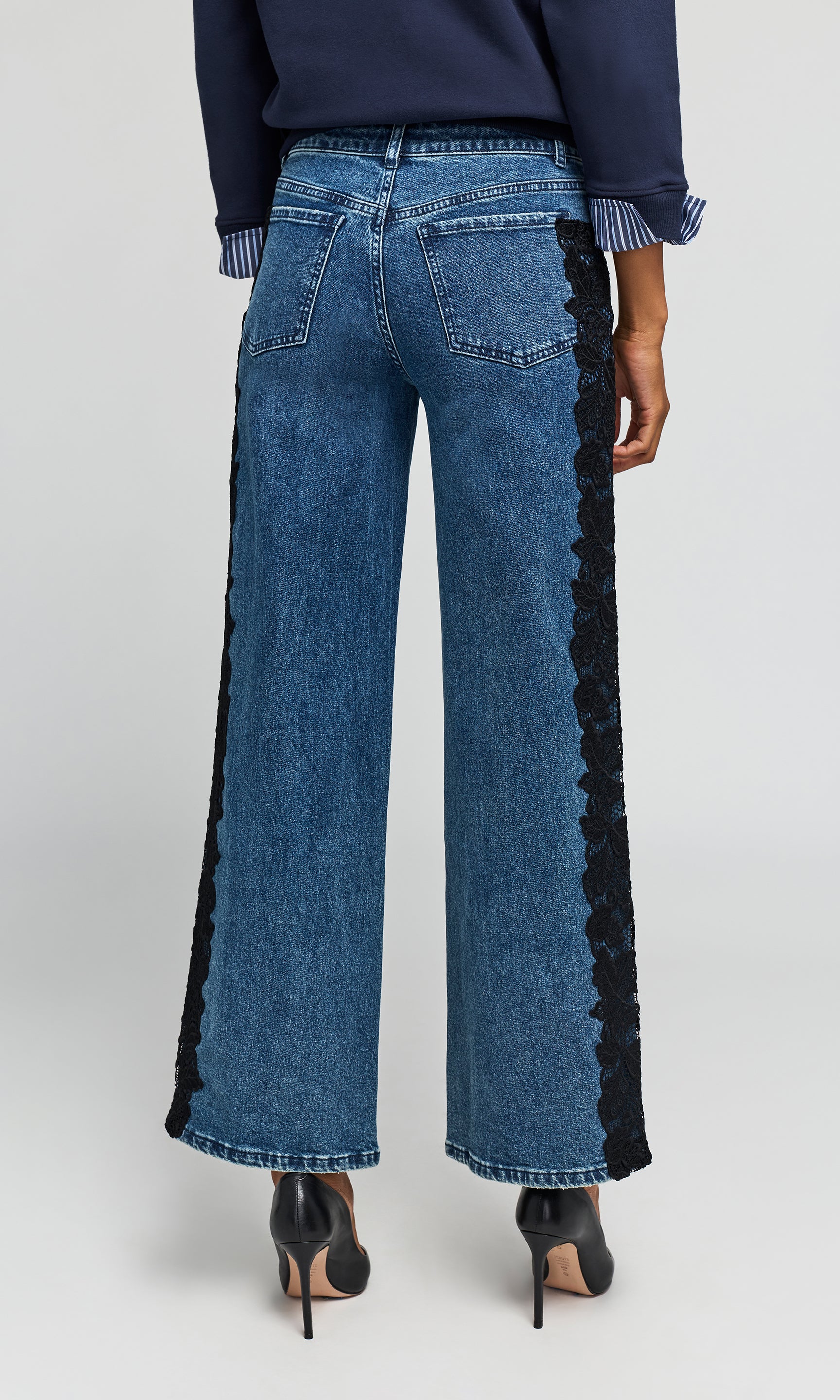 Back view of model wearing a blue wide-leg jeans with black lace side panels, styled with a navy top and black heels.