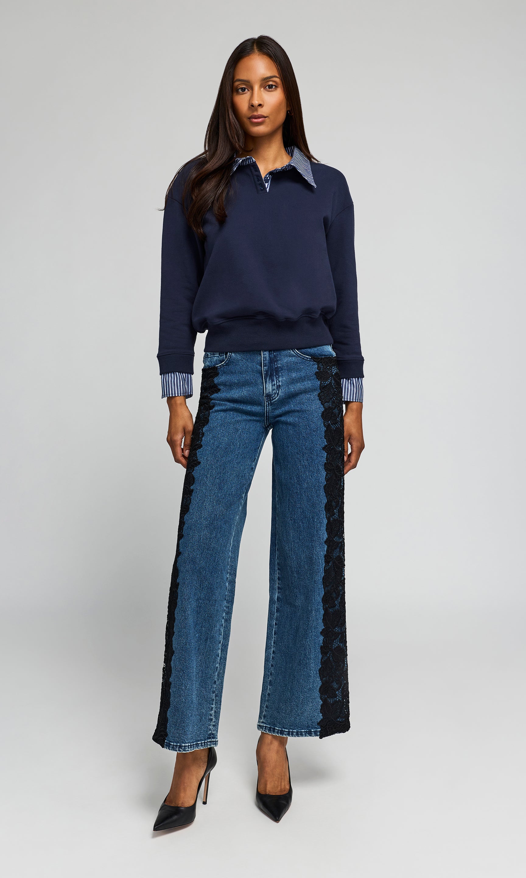 Model wearing a navy long-sleeve polo-style top with a light blue collar and striped cuffs, paired blue jeans featuring black lace side panels.