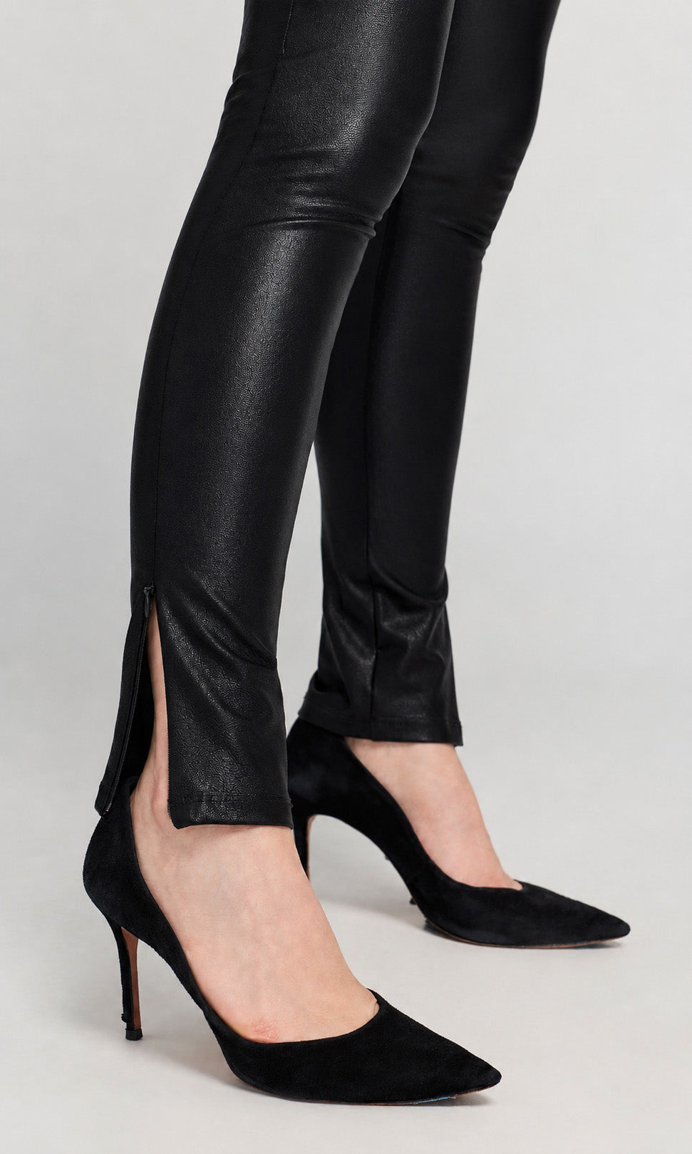 Close-up of black faux-leather slim-fit pants with side slits and black pointed-toe high heels.