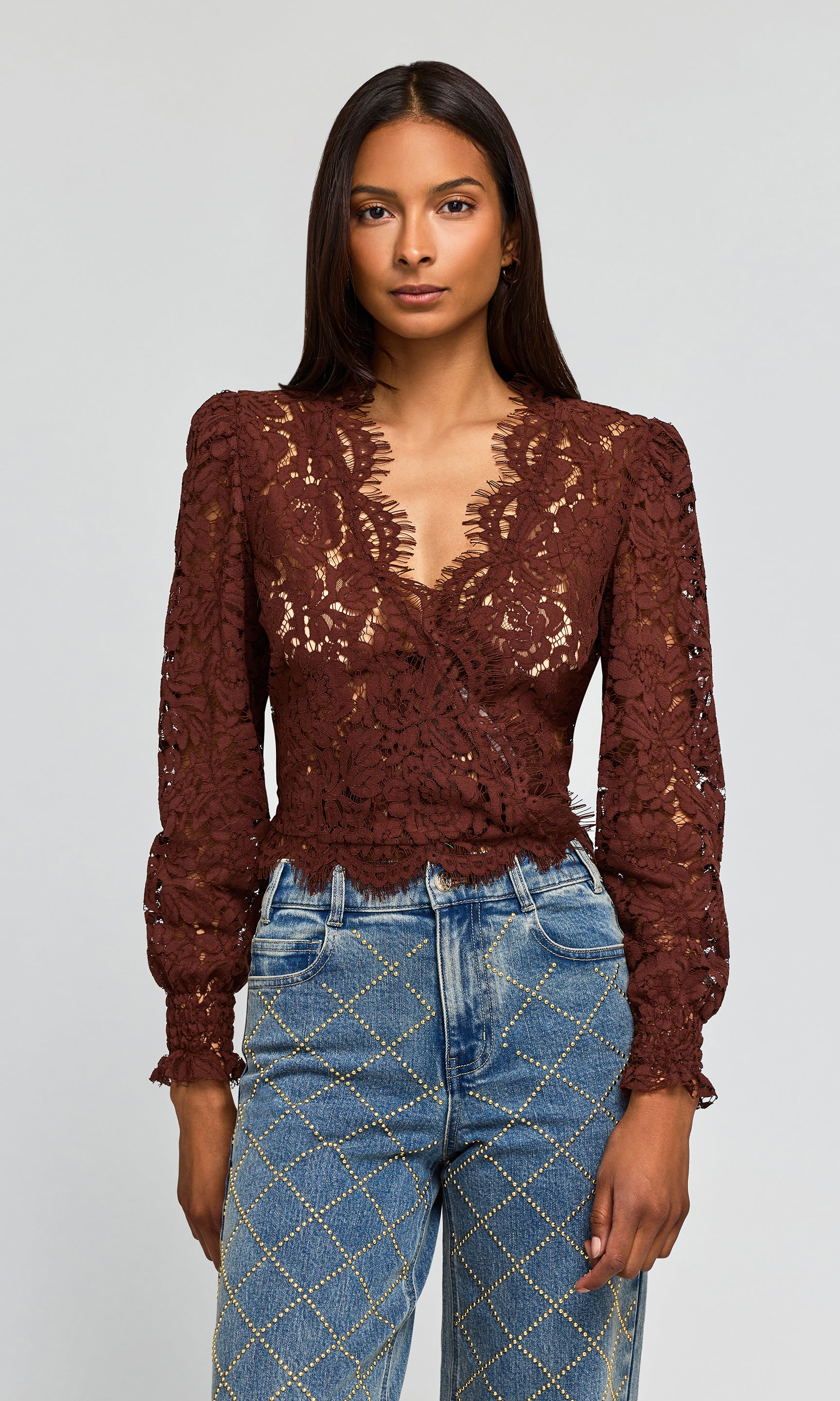 Model wearing a dark brown lace long-sleeve wrap top paired with blue jeans featuring a gold diamond pattern.