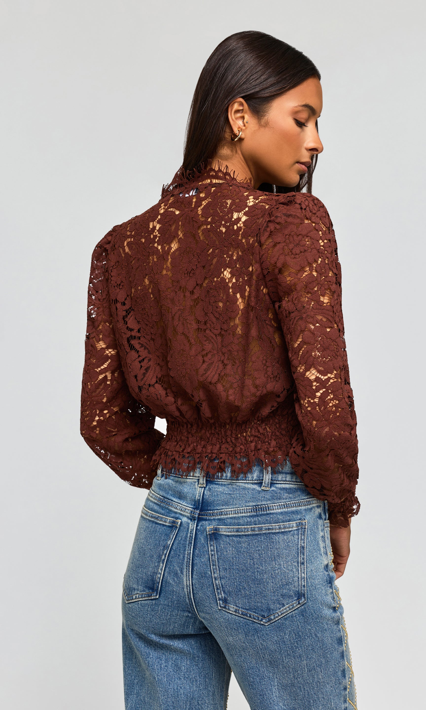 Back view of model wearing a dark brown lace long-sleeve crop top and blue jeans.