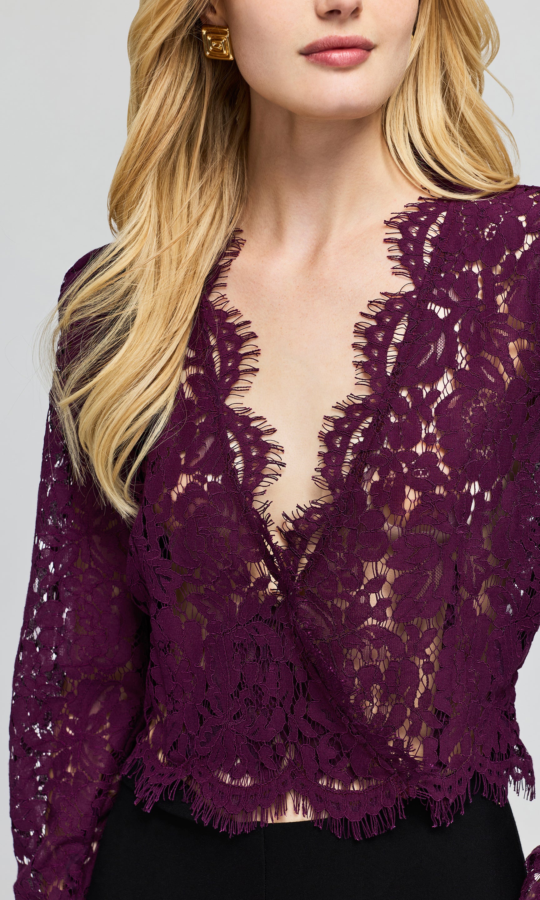 Close-up of a deep purple lace long-sleeve top with a deep V-neckline and fringed hem, paired with black bottoms.