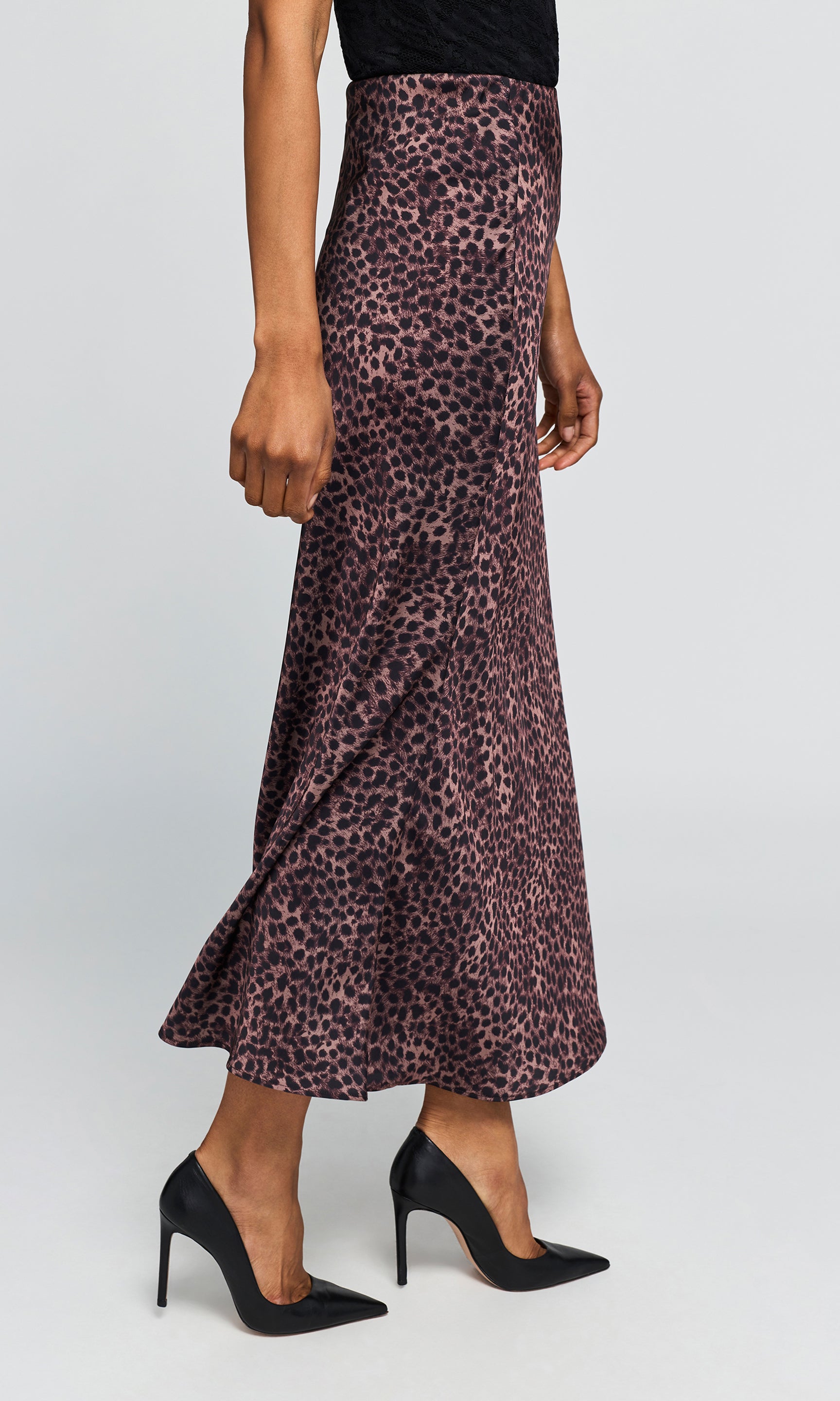 Side view of model wearing a high-waisted, floor-length leopard print skirt, paired with black pointed-toe heels on a plain background.