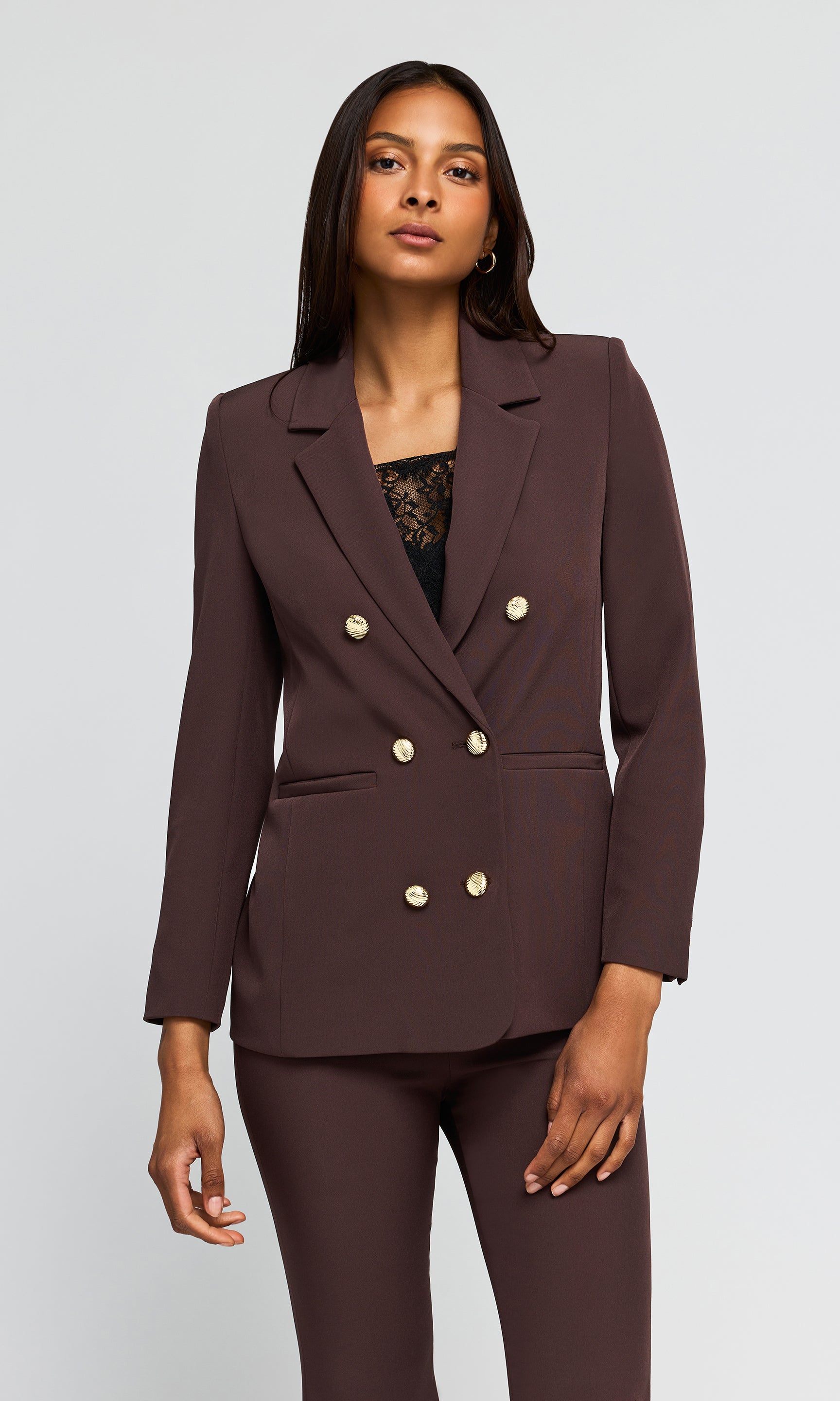 Model wearing a dark brown double-breasted blazer with gold buttons and matching trousers.