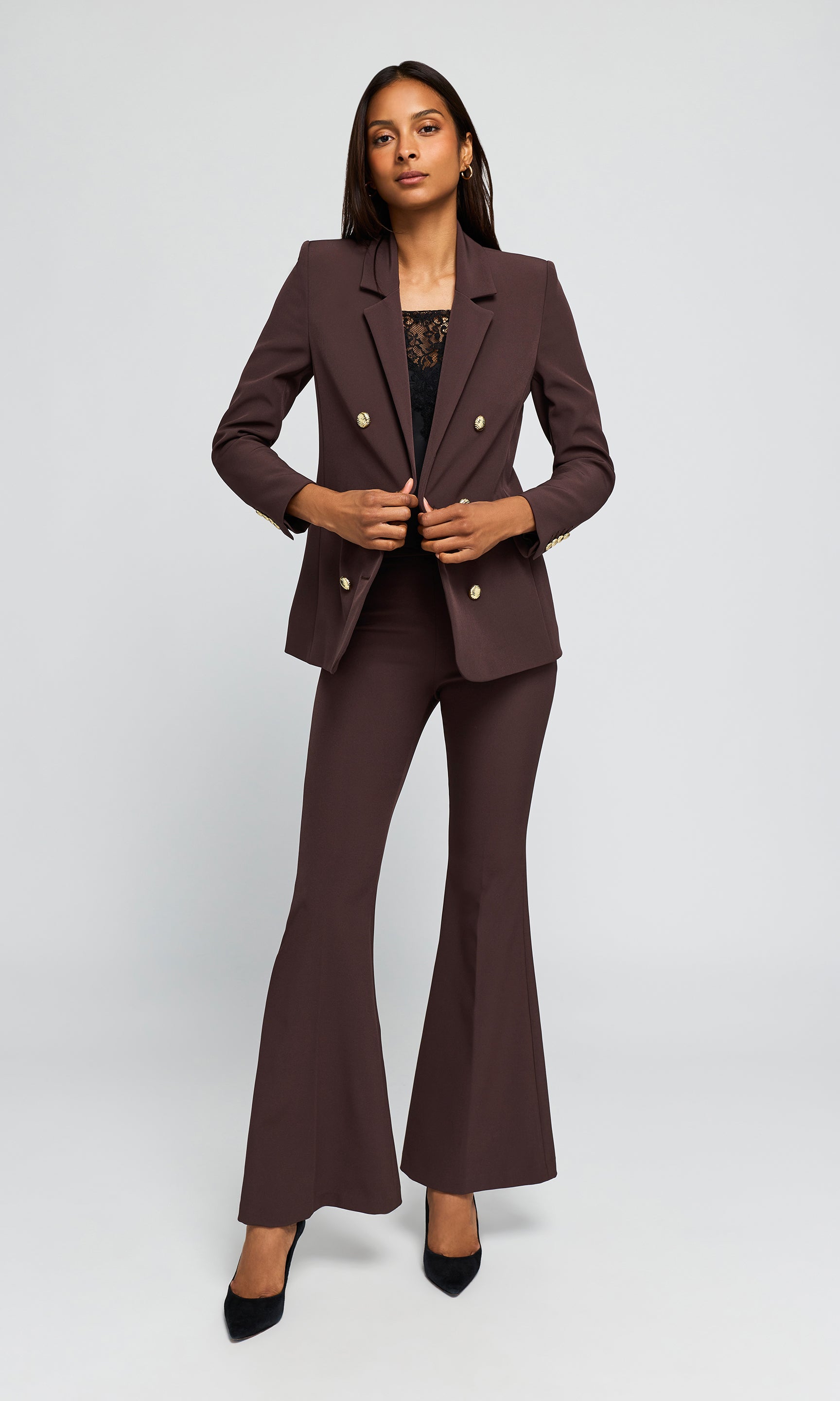 Model wearing a dark brown double-breasted blazer and matching flared trousers with gold buttons, paired with black heels.