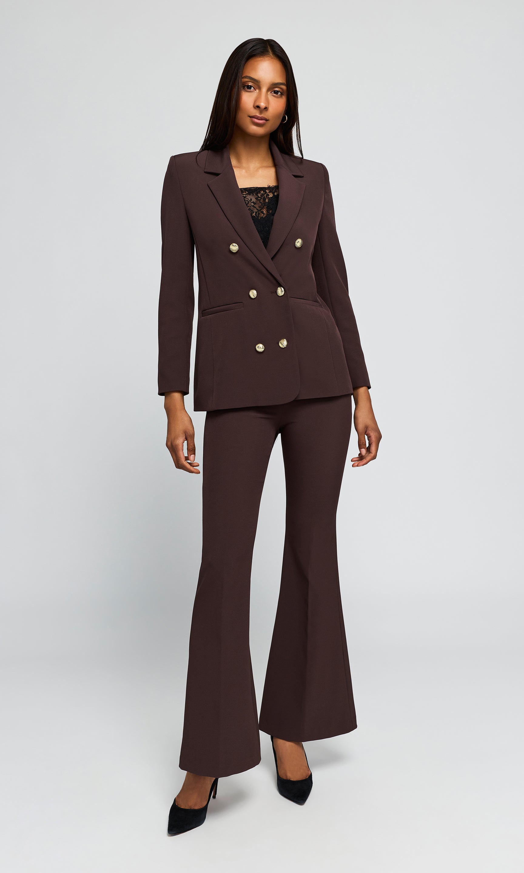 A woman modeling a dark brown double-breasted blazer with gold-tone buttons and matching flared trousers.
