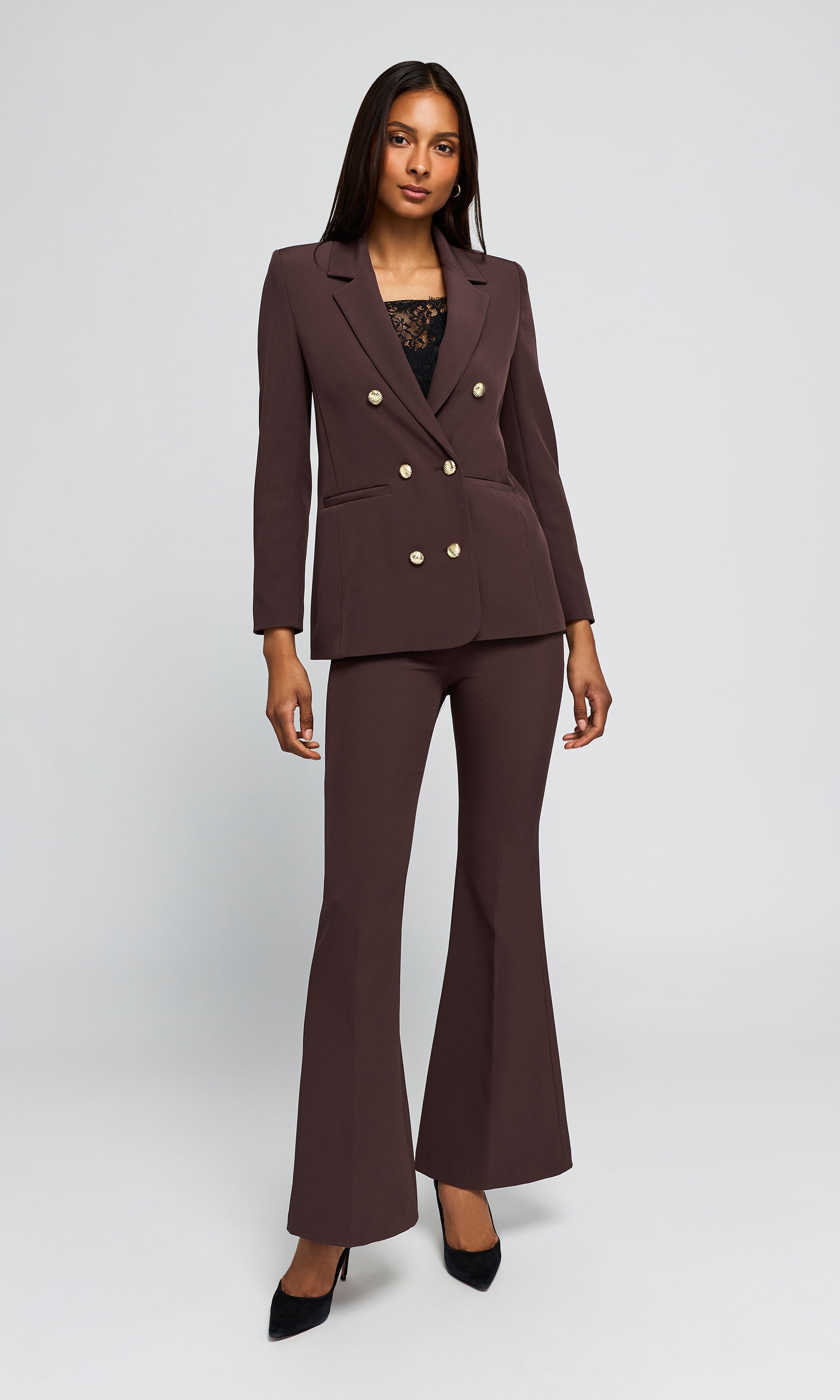Model wearing a dark brown double-breasted blazer and matching flared trousers with gold-tone buttons, paired with black pointed-toe heels.