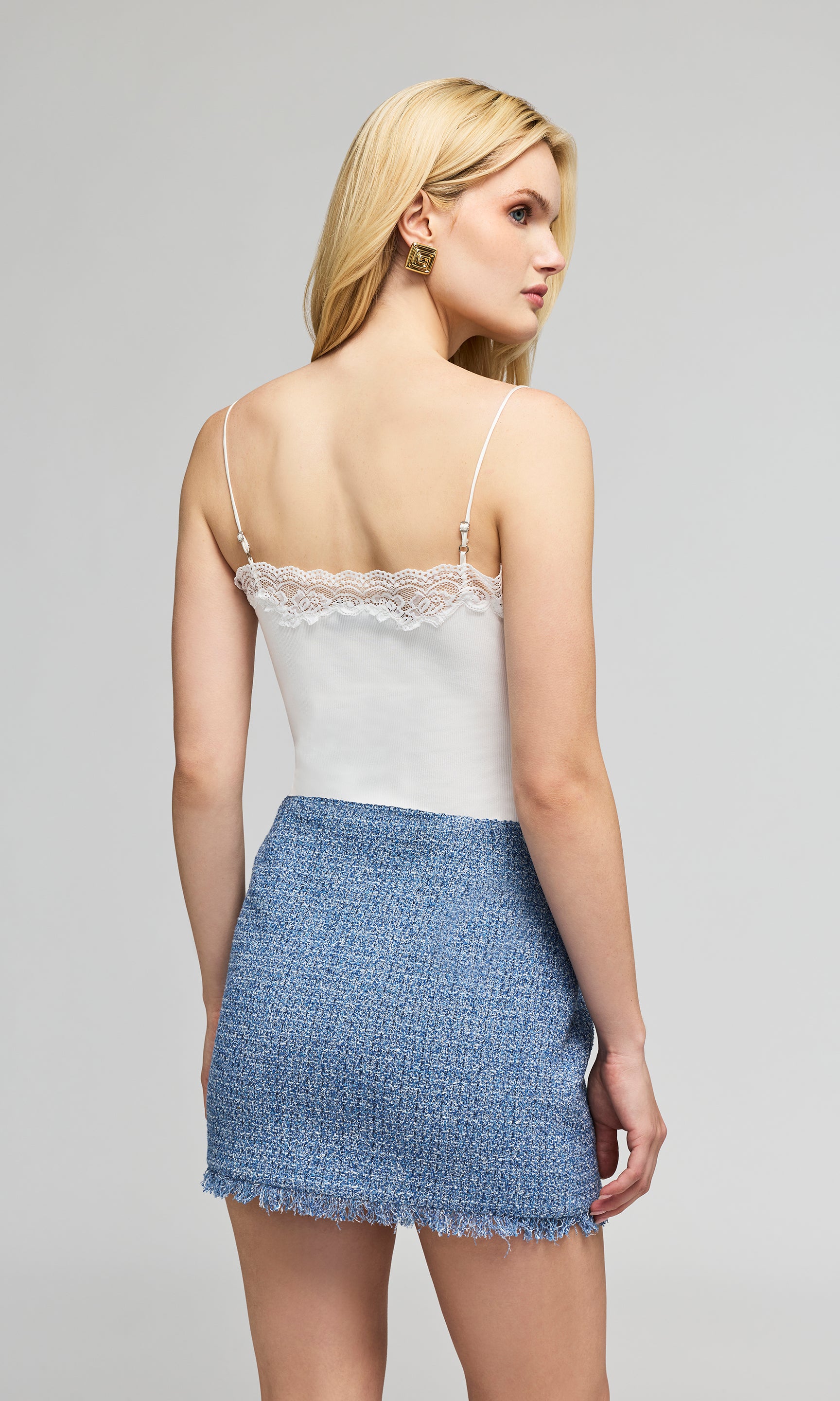Back view of model wearing a white camisole with lace trim and a blue tweed mini skirt, on a plain background.