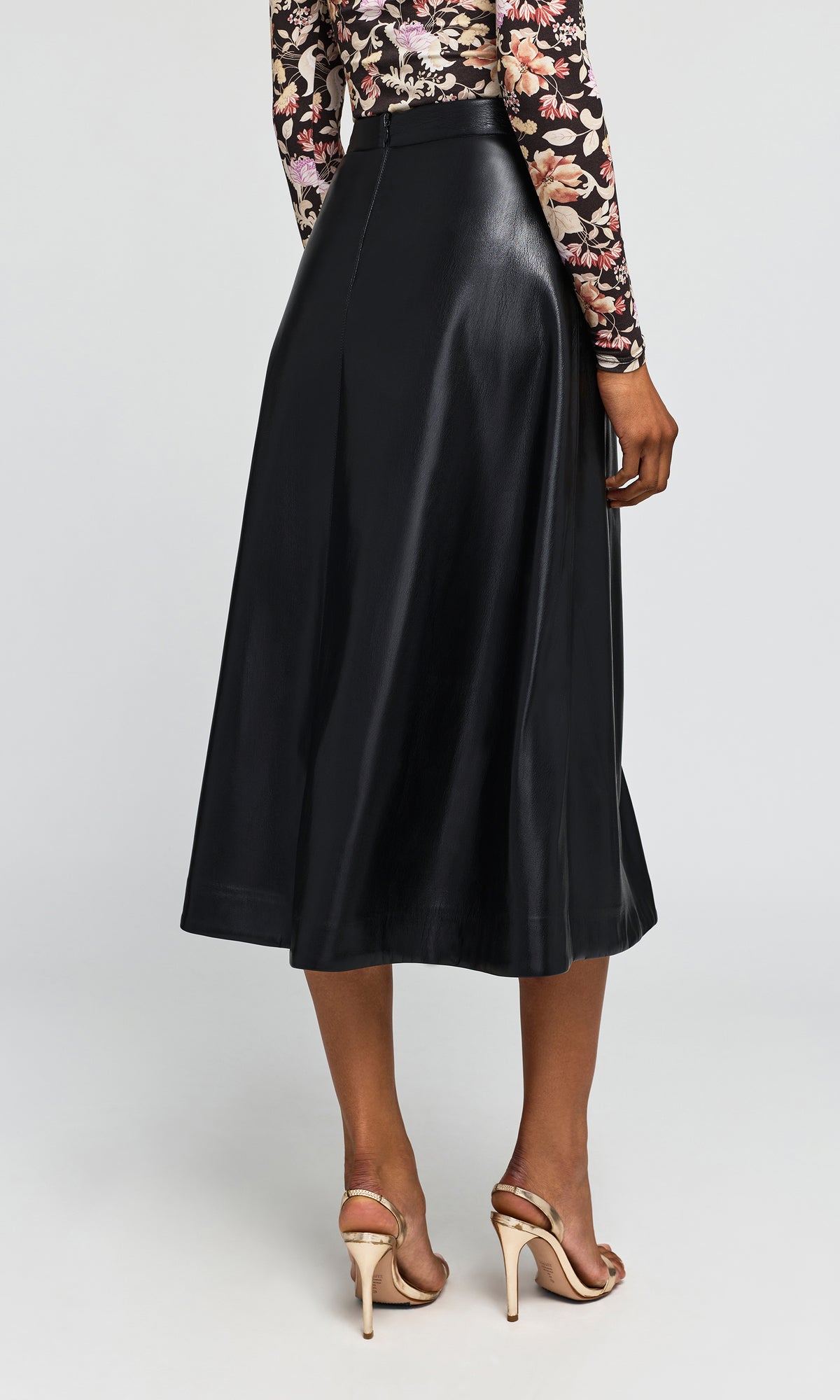 Back view of model wearing a black midi skirt with a satin-like sheen, paired with a floral long-sleeve top.
