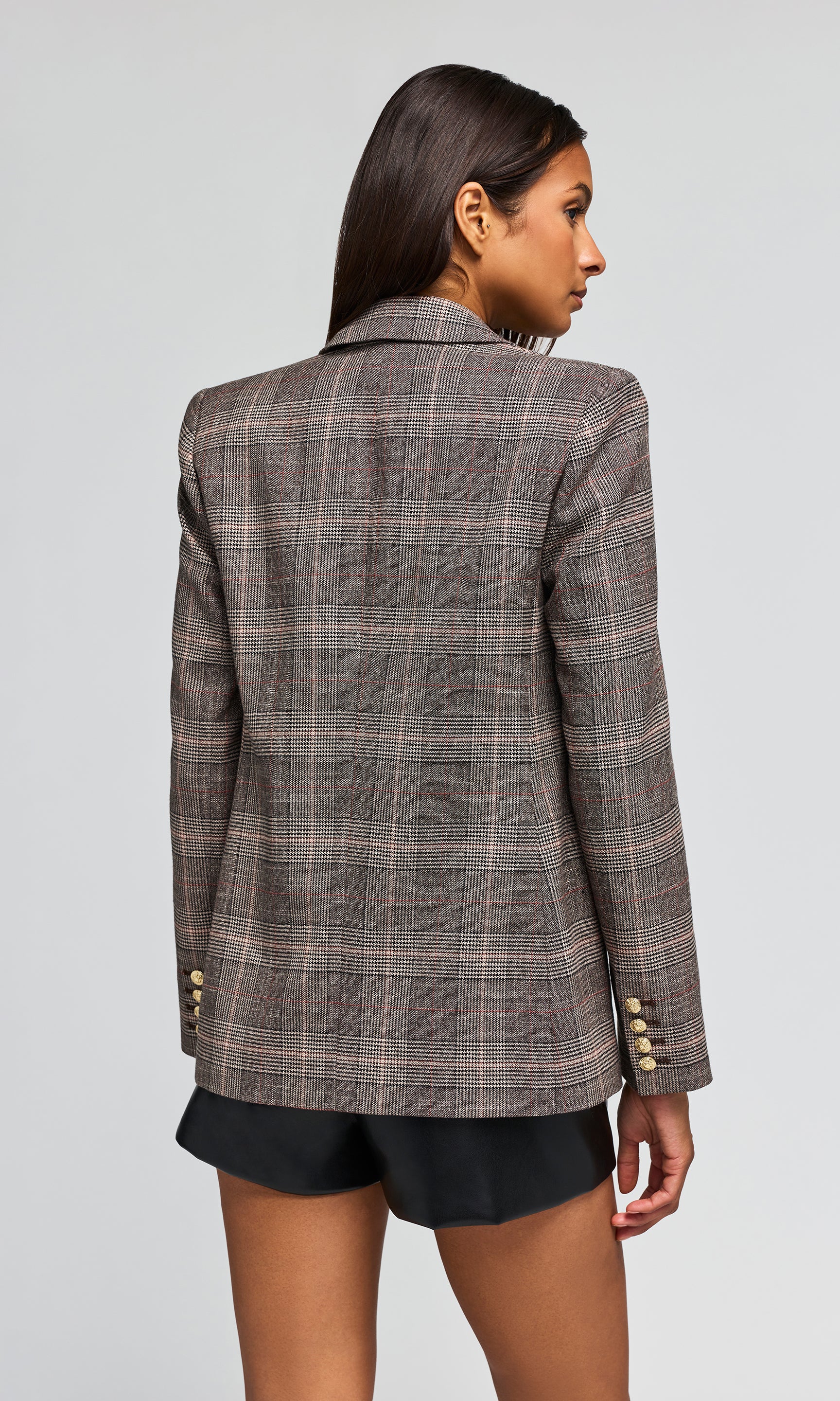 Back view of model wearing a double-breasted plaid blazer in brown and gray tones, paired with a dark brown ruffled top and black shorts.