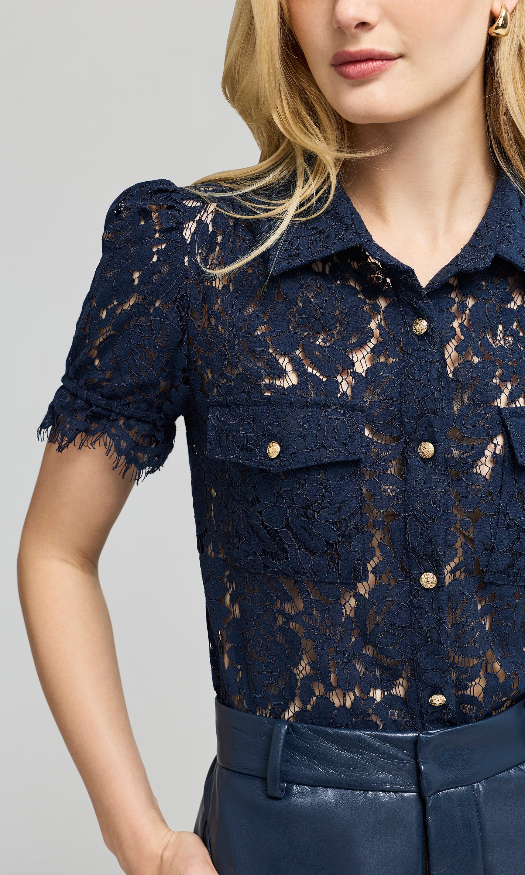 Close-up of a navy blue lace short-sleeve button-up blouse with gold-tone buttons and chest pockets, on a plain background.