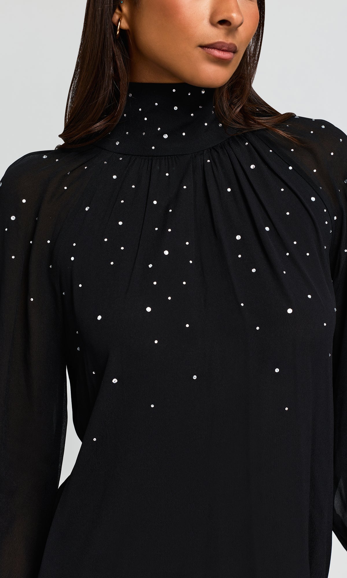 A close-up of a woman wearing a black long-sleeve blouse with a high mock neck and scattered small white rhinestone embellishments.