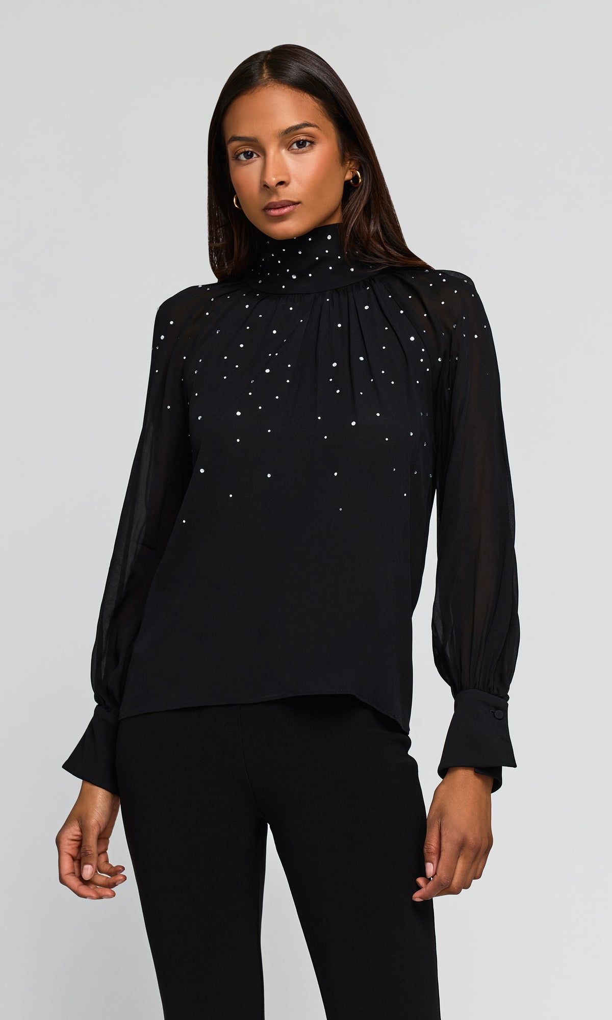 Model wearing a black long-sleeve blouse with sheer mesh sleeves and scattered rhinestone embellishments on the chest.