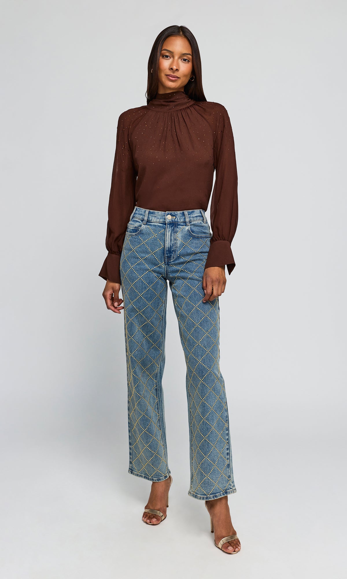Model wearing a brown long-sleeve mock-neck top and blue jeans with a gold geometric pattern.