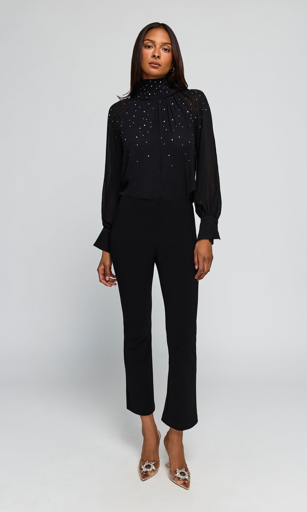 Model wearing a black long-sleeve blouse with sparkling embellishments across the chest and black cropped trousers.