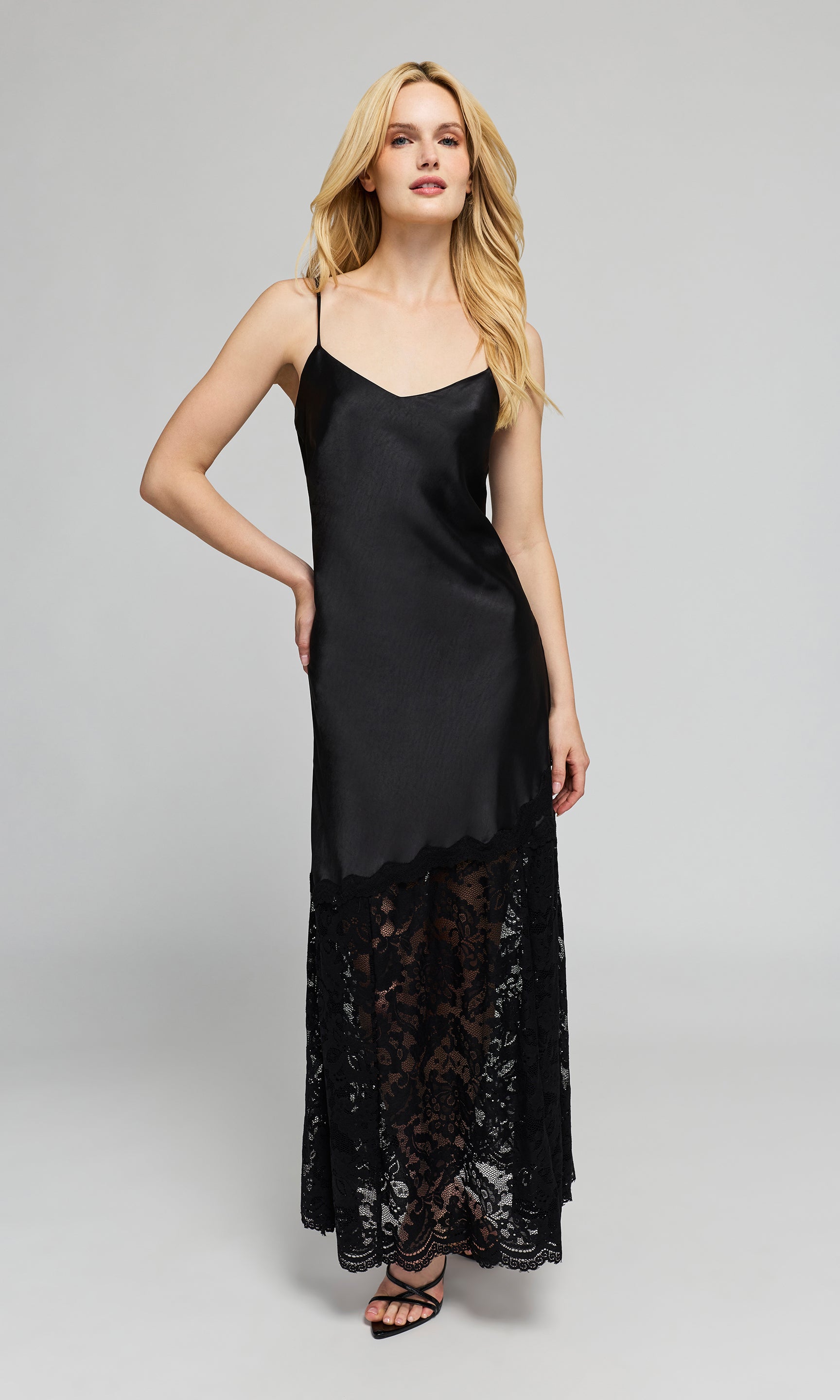 Model wearing a black satin slip dress with thin straps and a black lace hem, on a plain background.
