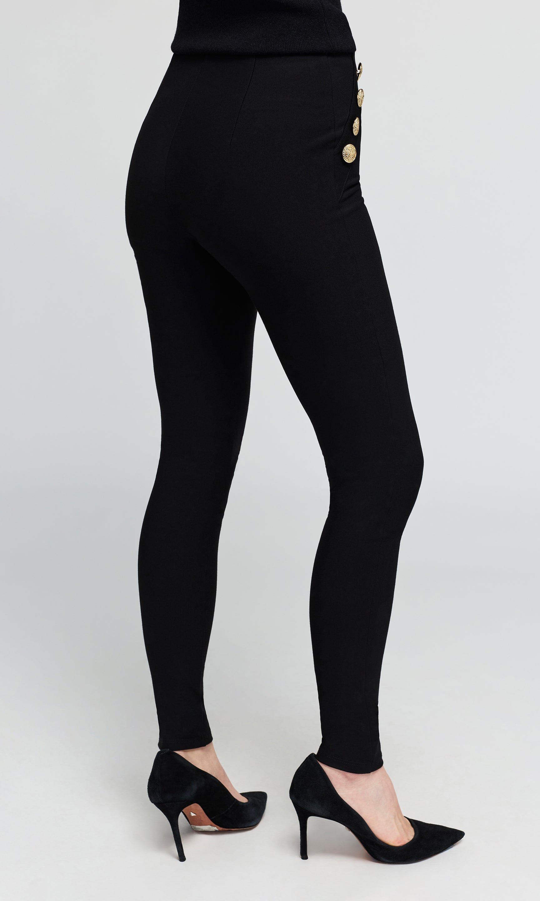 Black high-waisted leggings with three gold buttons on the side, shown on a model from the back wearing black high heels.