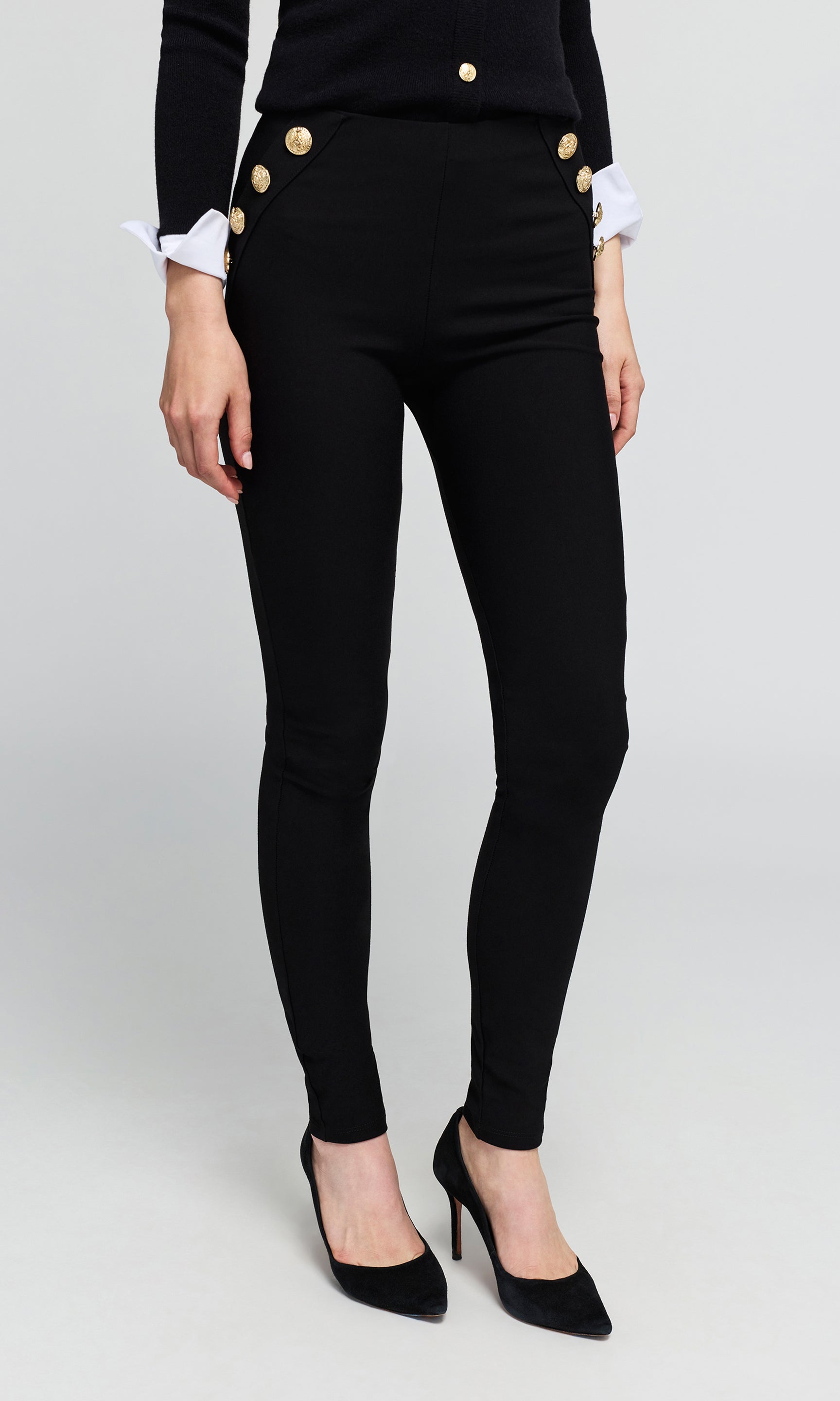 Black skinny pants with decorative gold buttons on the hips and cuffs, modeled with a black top and black heels.