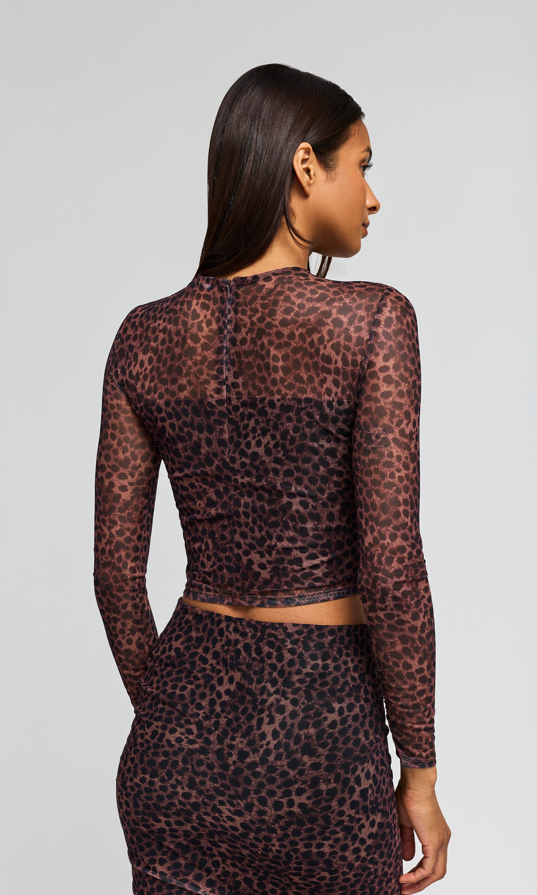 Back view of model wearing a leopard-print midi skirt and matching sheer long-sleeve crop top on a plain background.