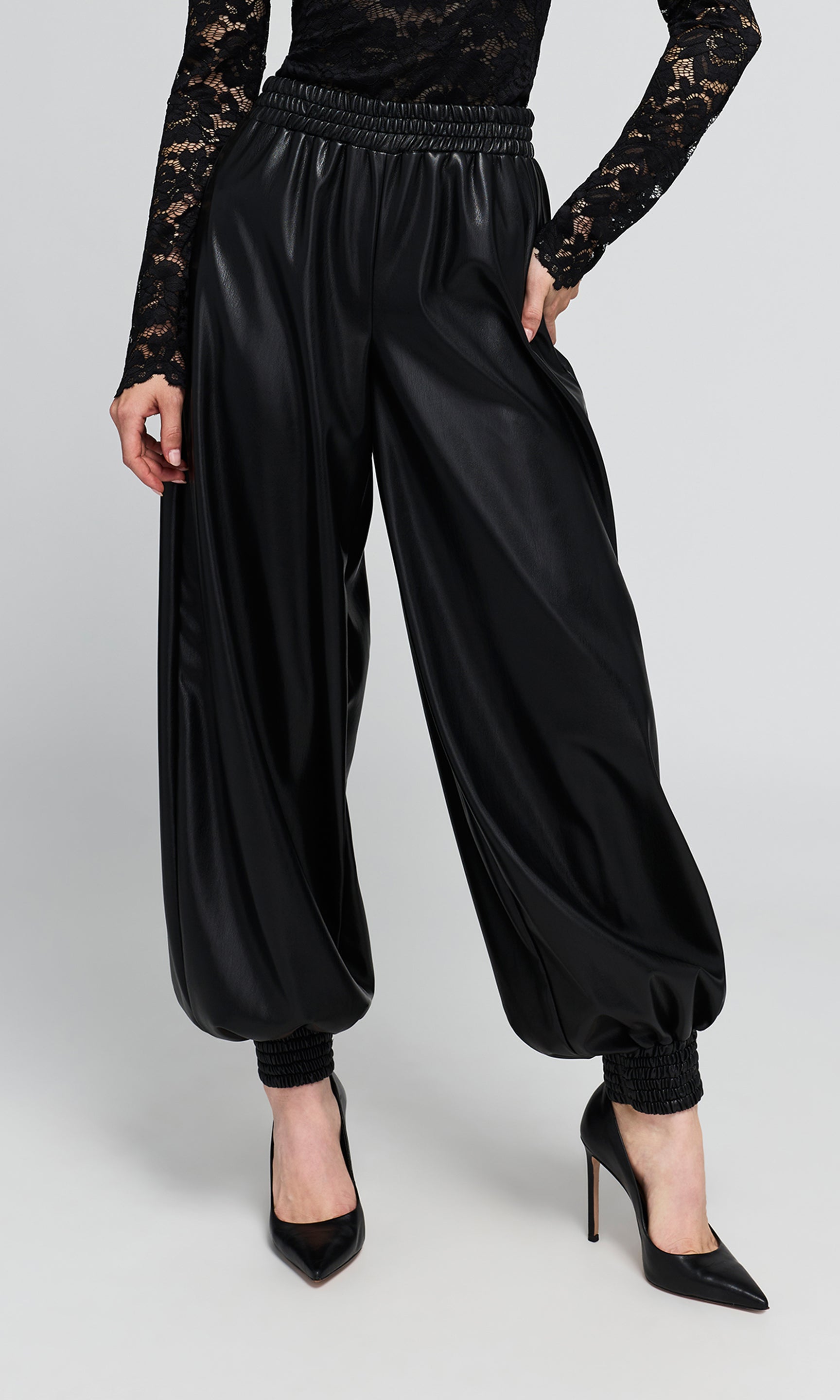 Black vegan-leather, wide-leg harem pants with an elastic waistband, and gathered cuffs, shown on a model.