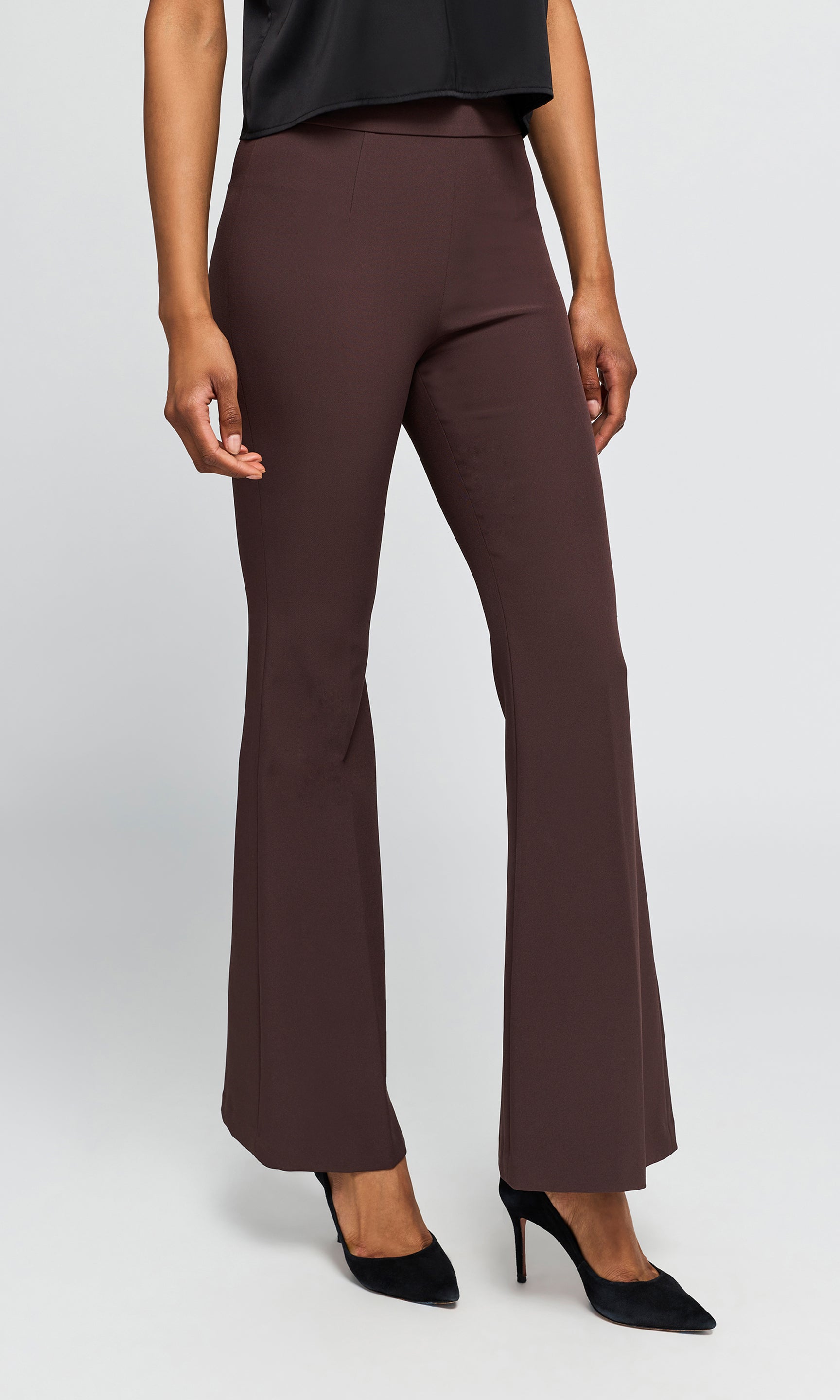 Side view of model wearing a pair of dark brown flared pants with black pointed-toe heels, on a plain background.