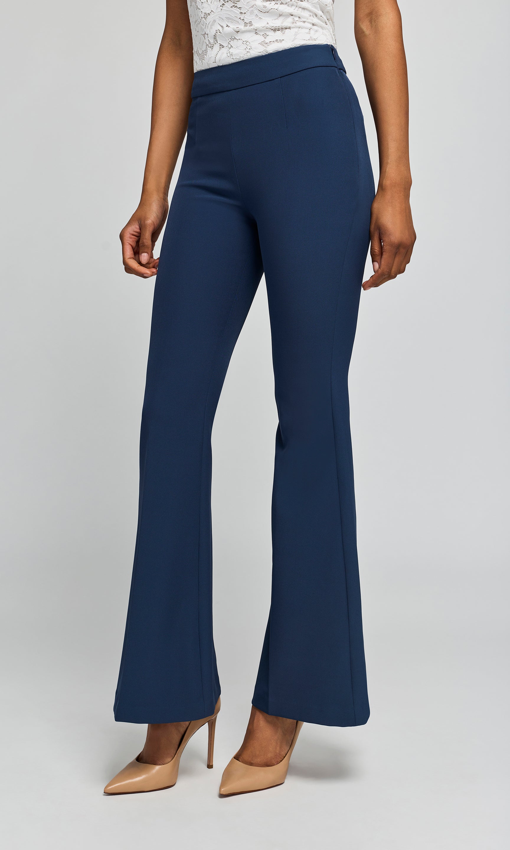 Side view of model wearing navy crepe pants with a white top and beige heels on a plain background.