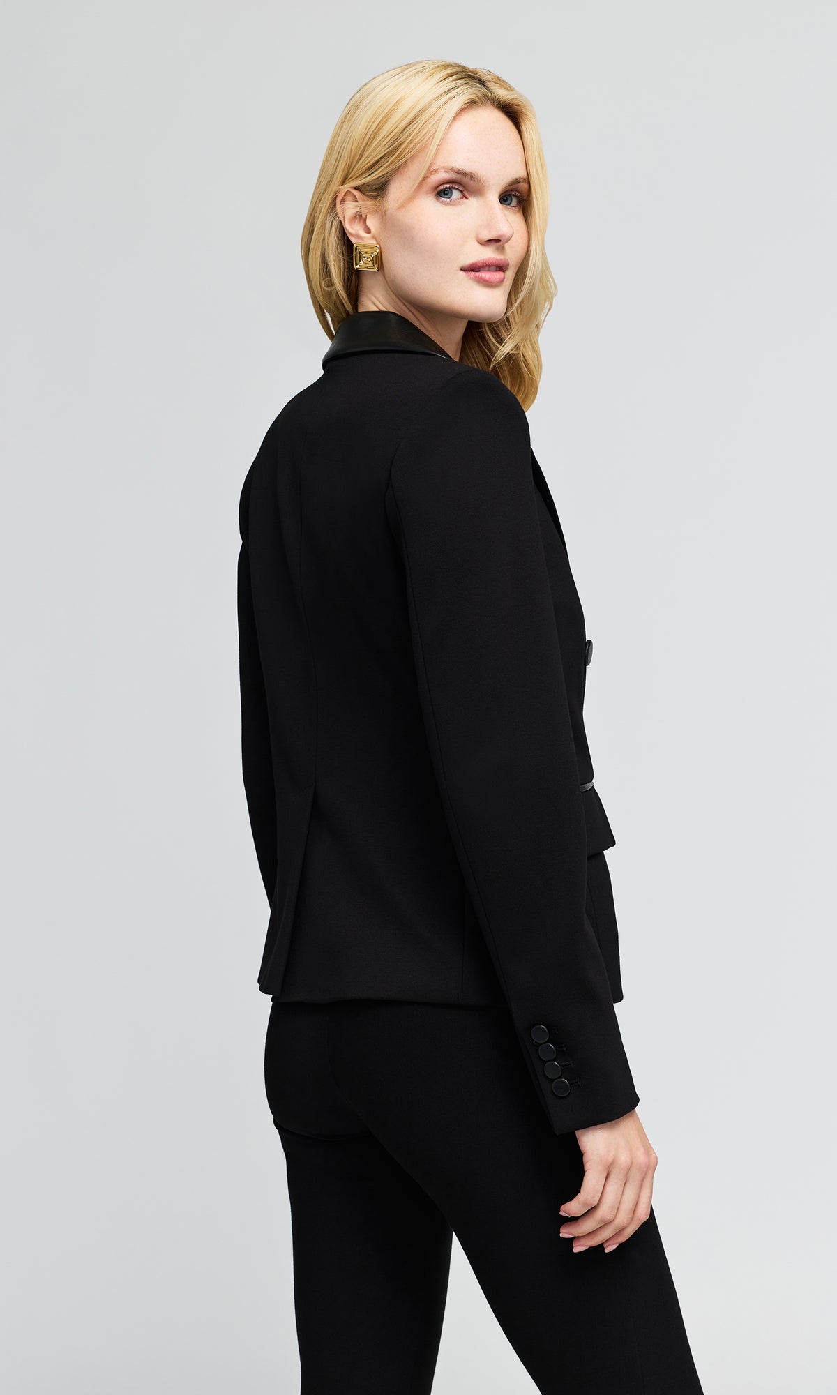3/4 back view of model wearing a black double-breasted blazer with structured shoulders and black pants.