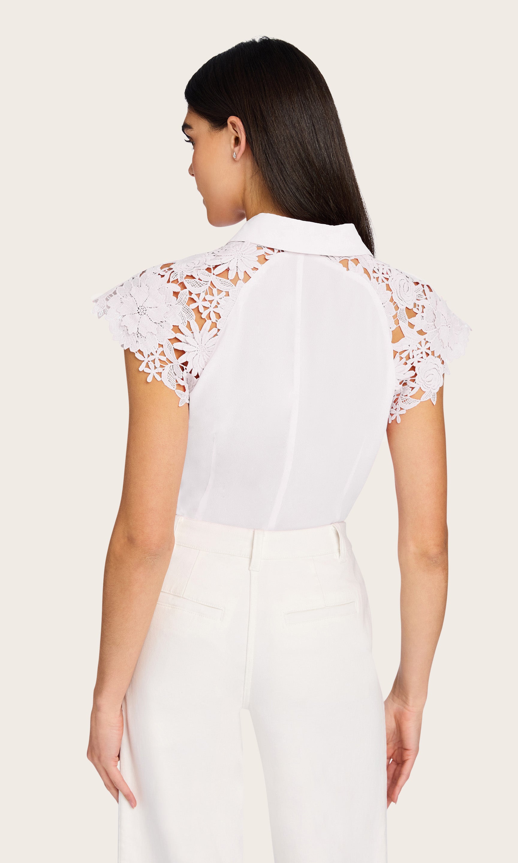 Back view of woman wearing a white blouse with lace details on a plain background