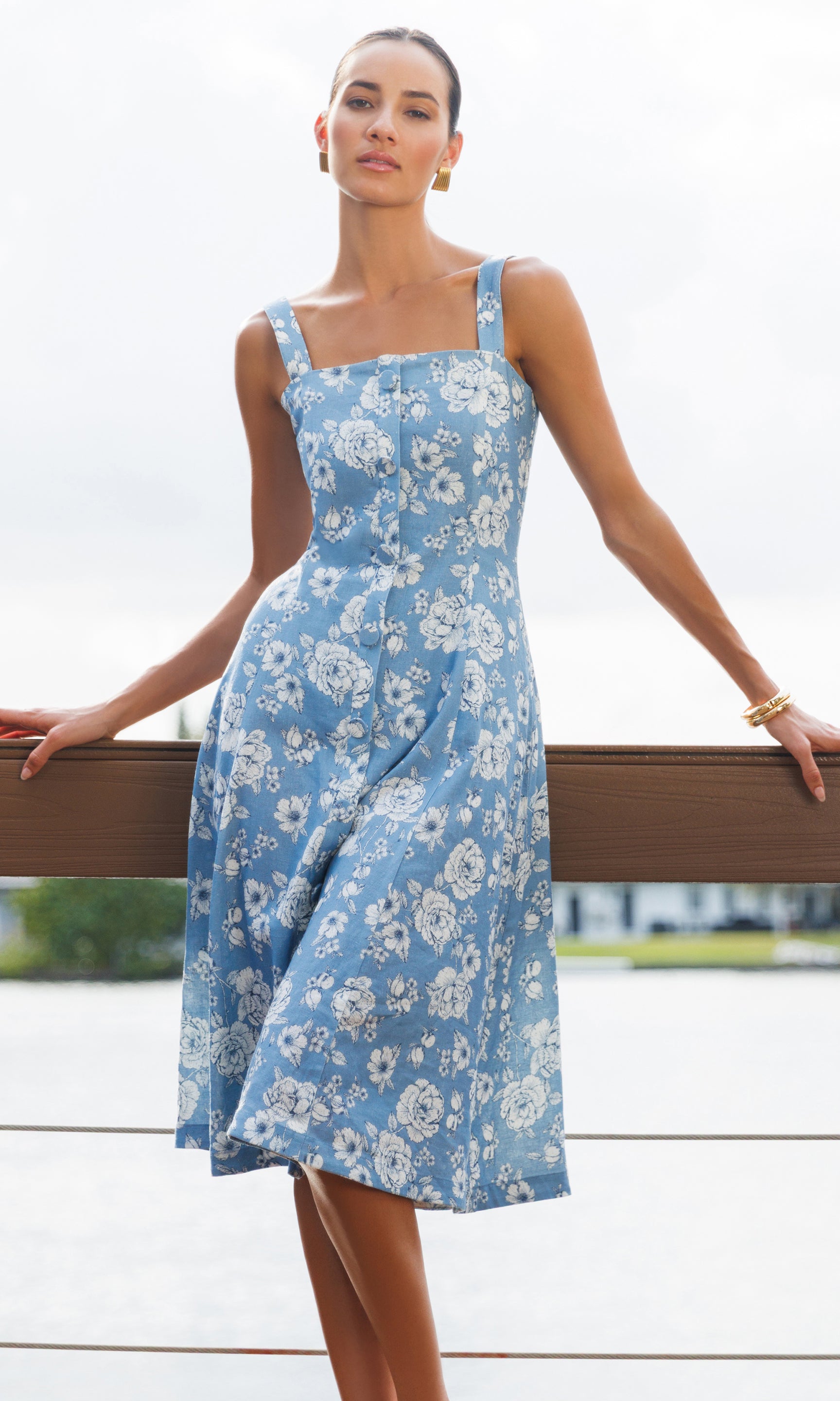 Woman wearing a blue floral dress standing by a waterfront.