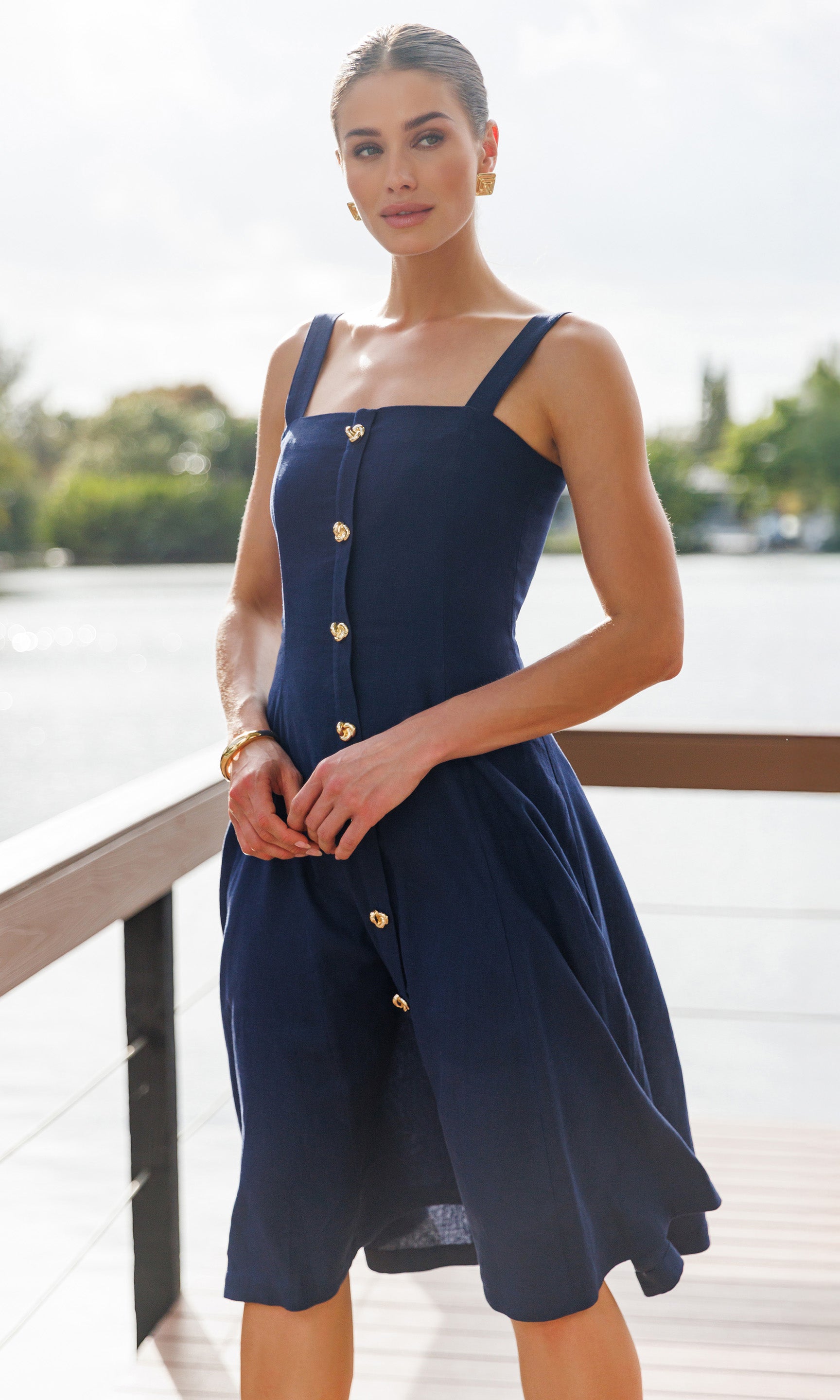 Woman wearing a navy dress with gold buttons by a waterfront