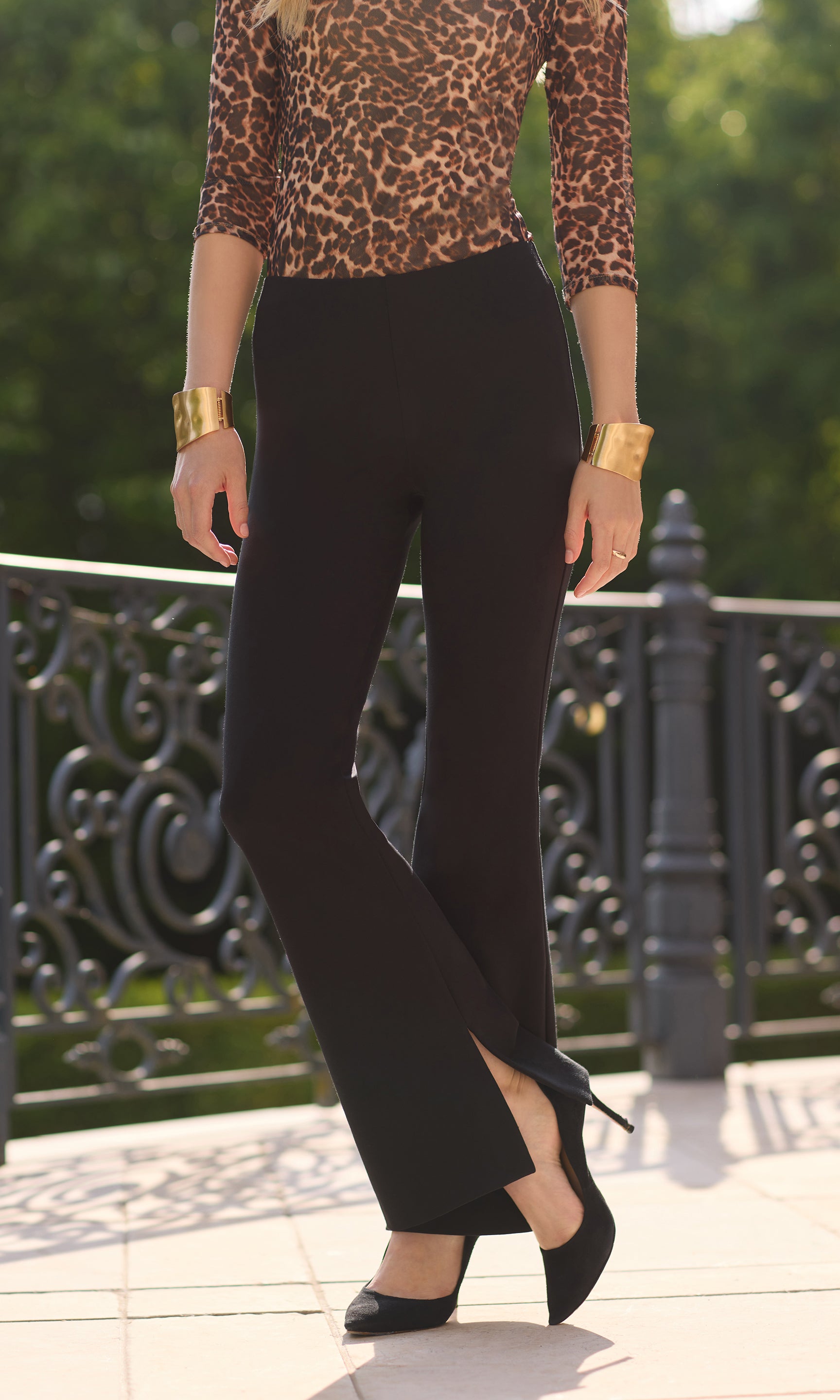 cropped image model outdoors in a patio wearing a leopard mesh blouse paired with the Murray leggings in black showcasing the wide leg fit with a slight slit on the side hems, with black heels