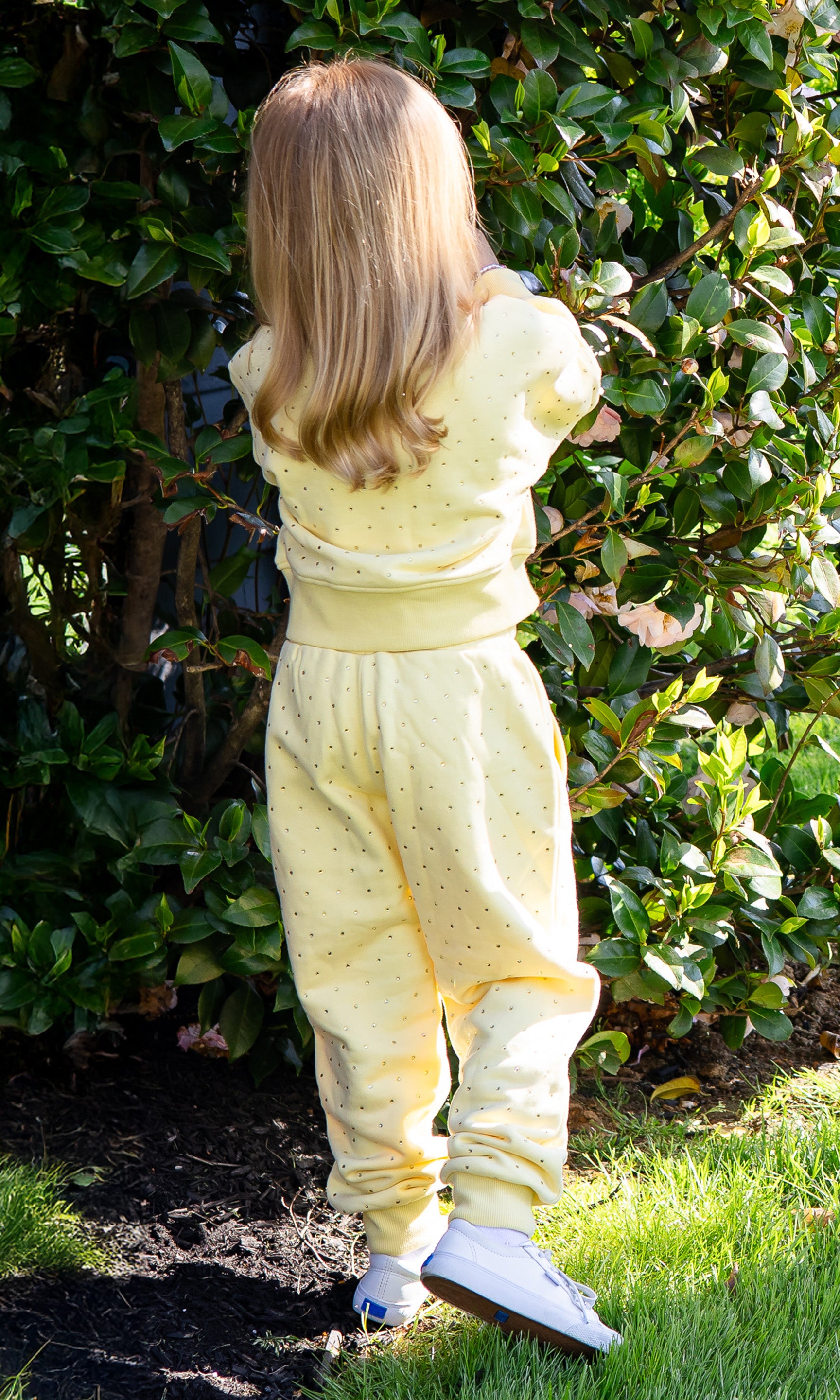Child wearing a yellow outfit standing in front of green bushes