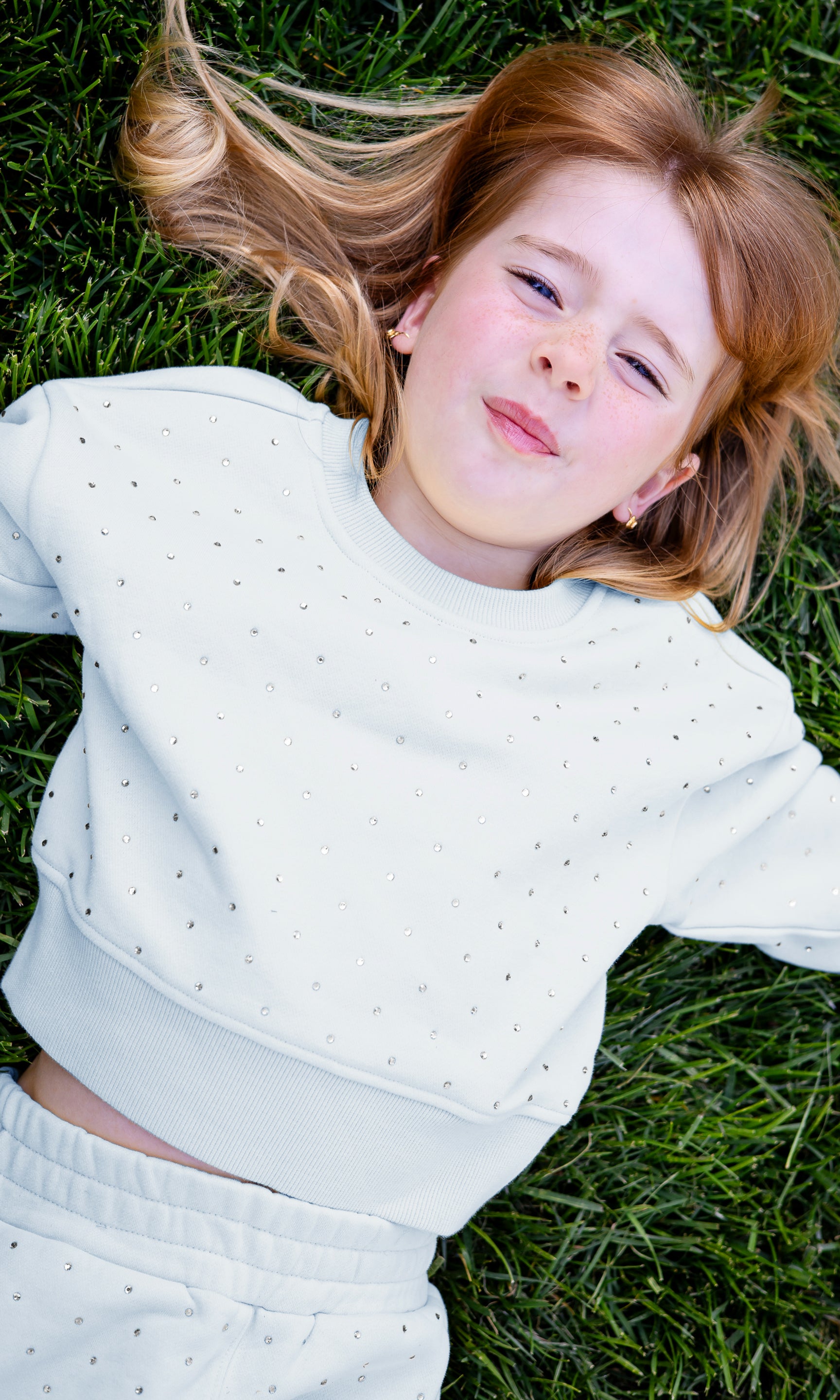 Young girl lying on grass wearing a light-colored outfit with crystals