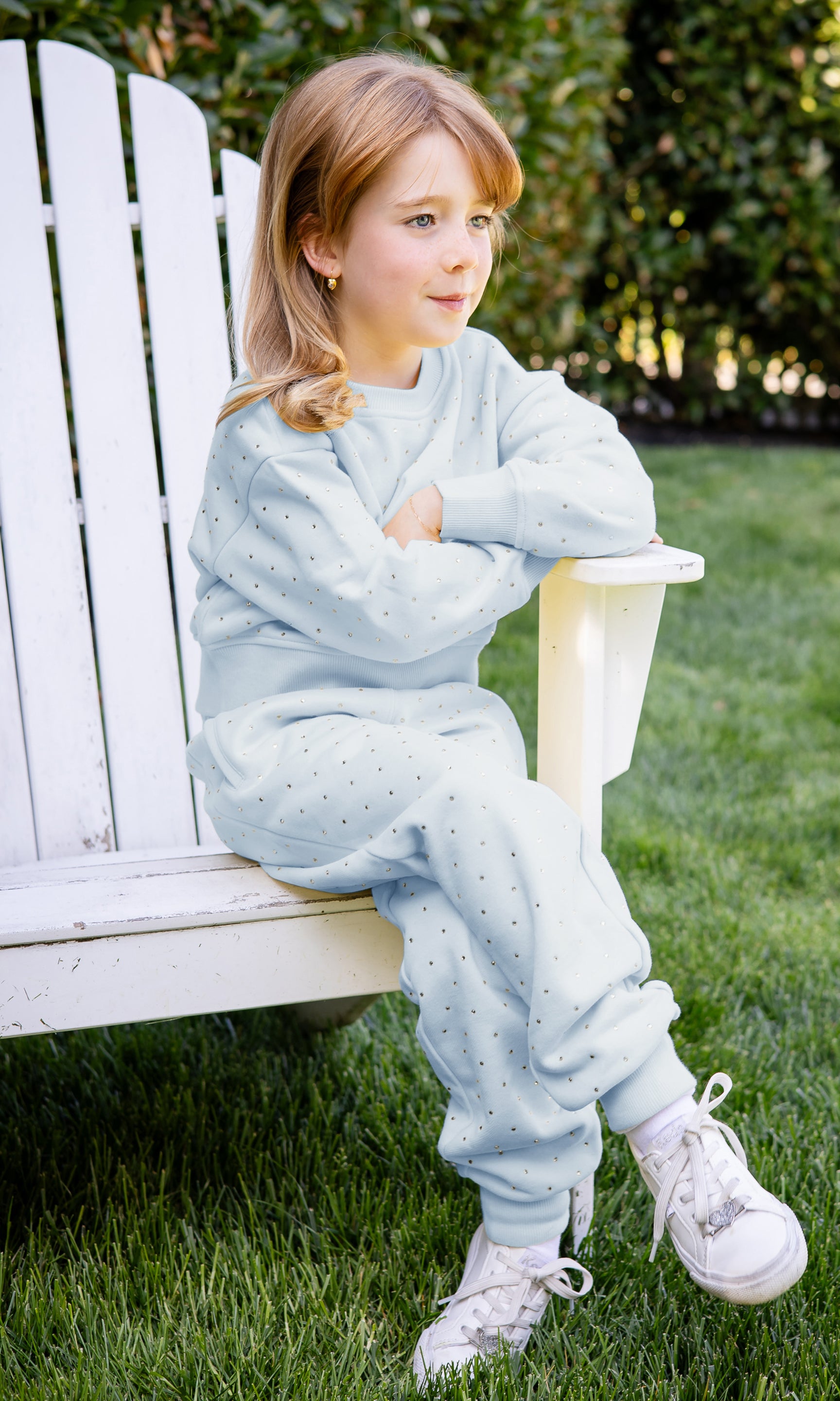 Child in light blue pajamas sitting on a white chair outdoors.
