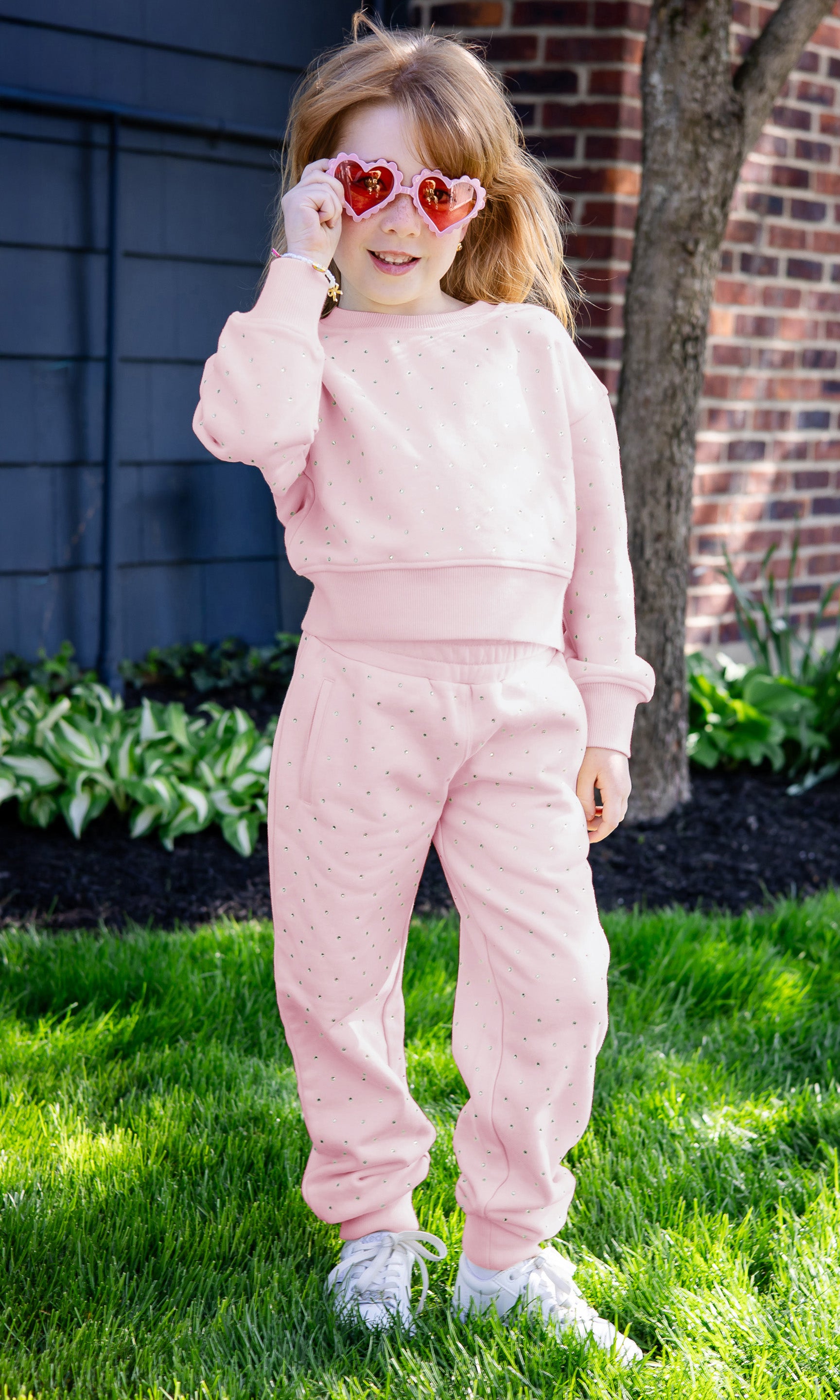 Child wearing a pink outfit with heart-shaped sunglasses outdoors.