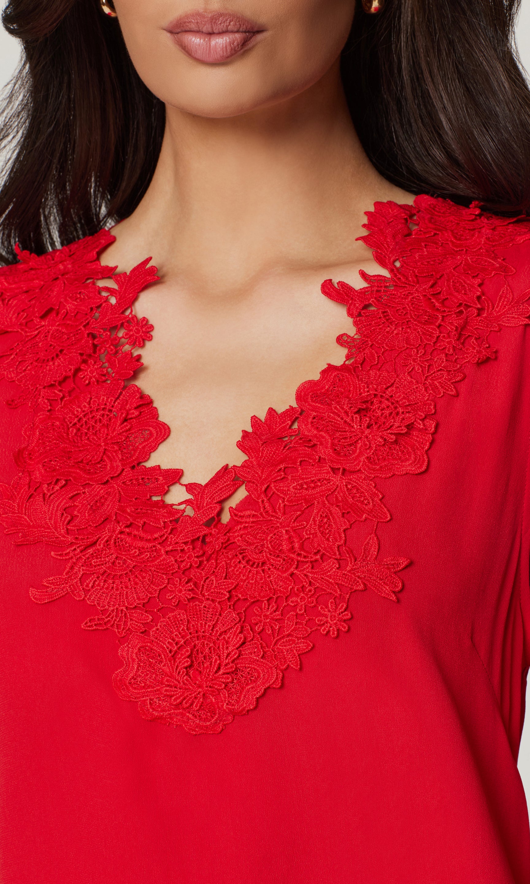 Close-up of red top with lace detail neckline worn by a model with a blurred background