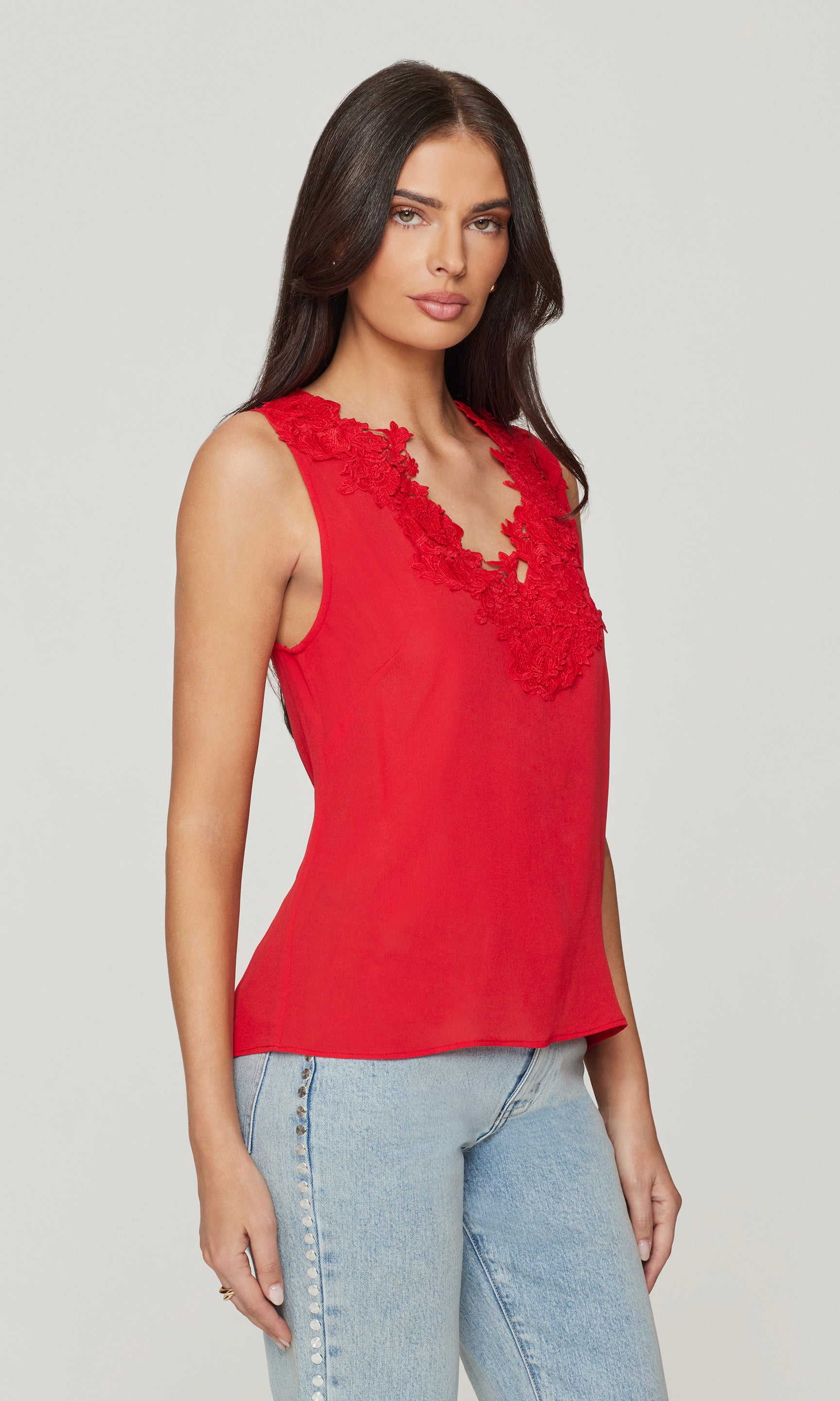 Side view of woman wearing a red sleeveless top with lace details on a plain background