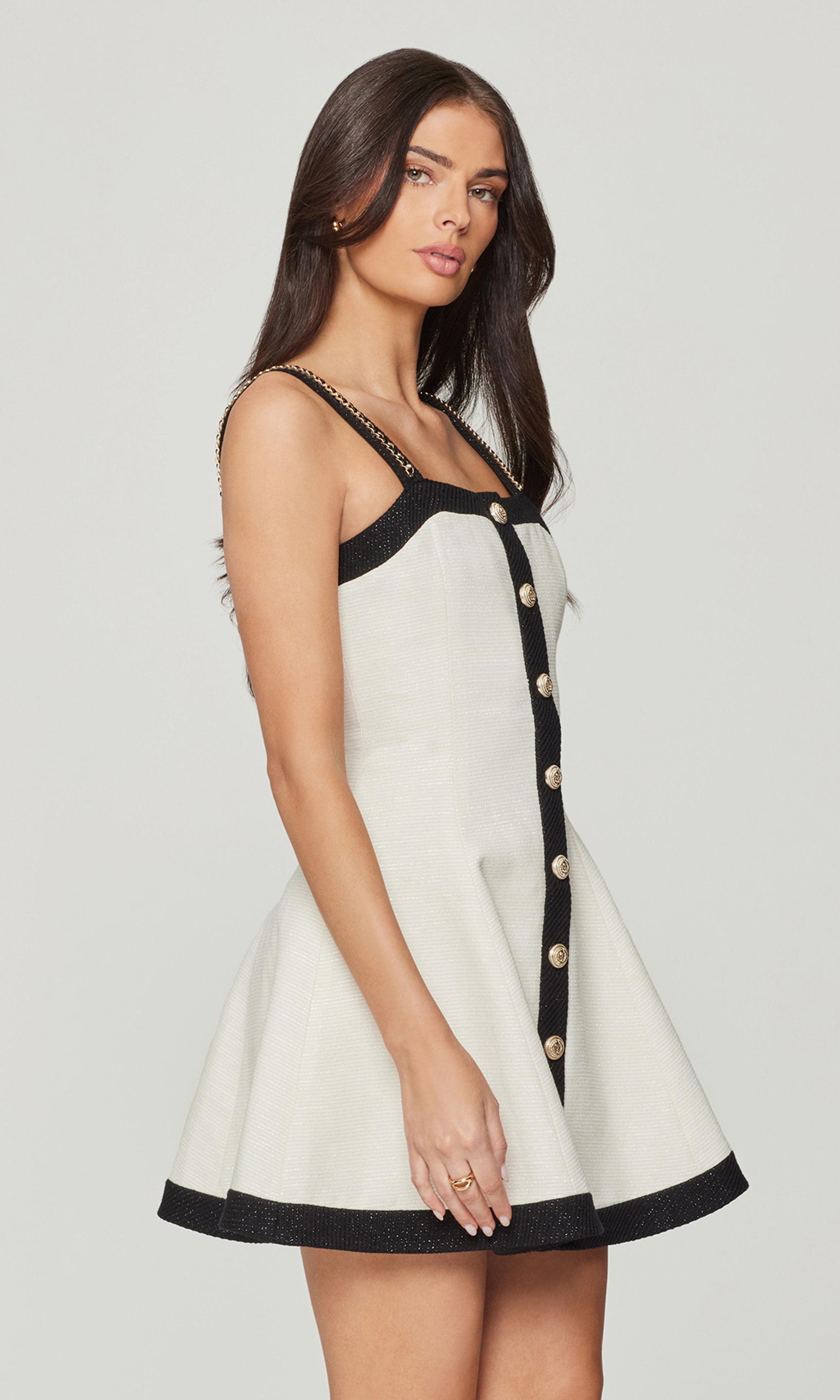 Side view of woman wearing a white dress with black trim and buttons on a plain background