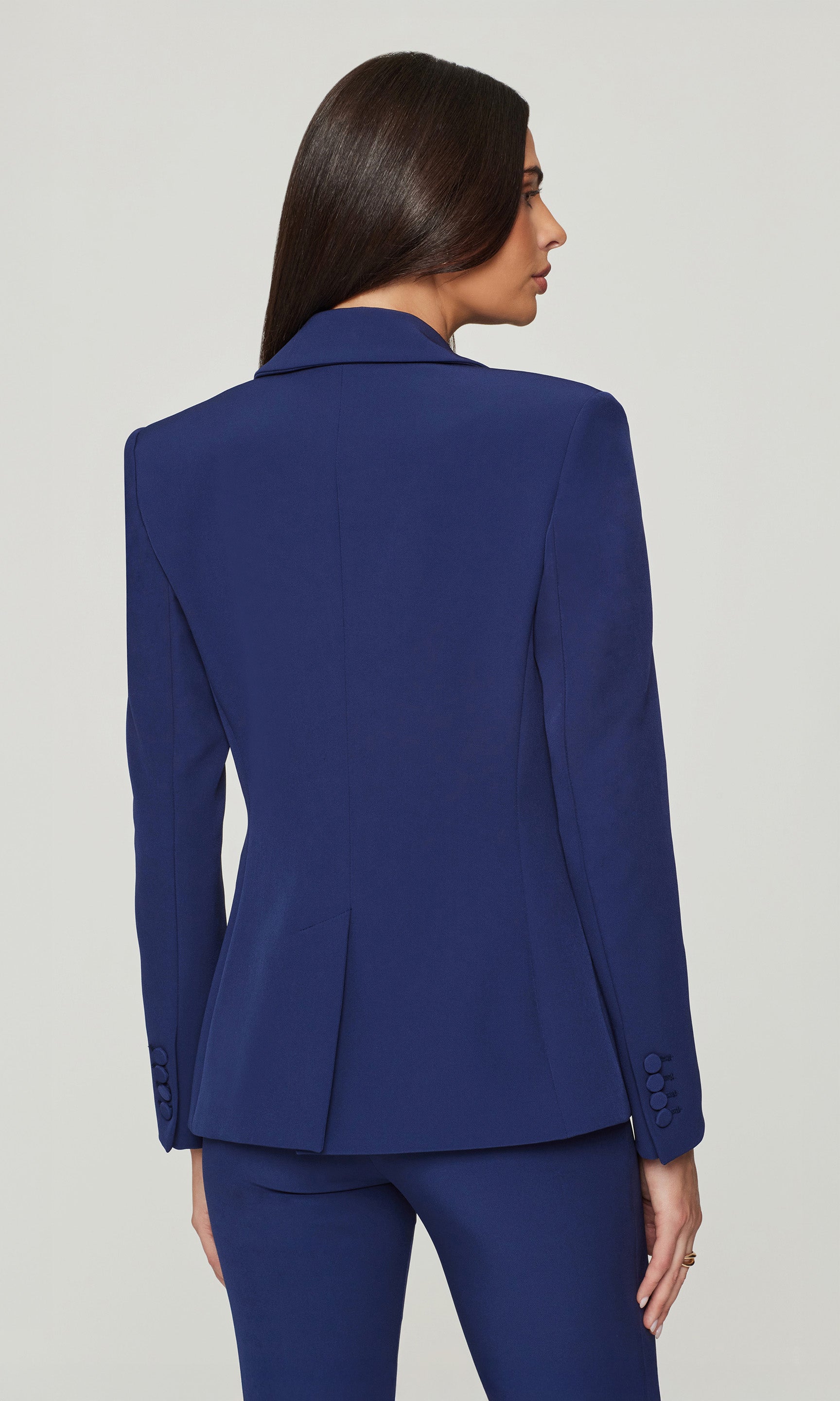 Back view of woman wearing a blue suit on a plain background